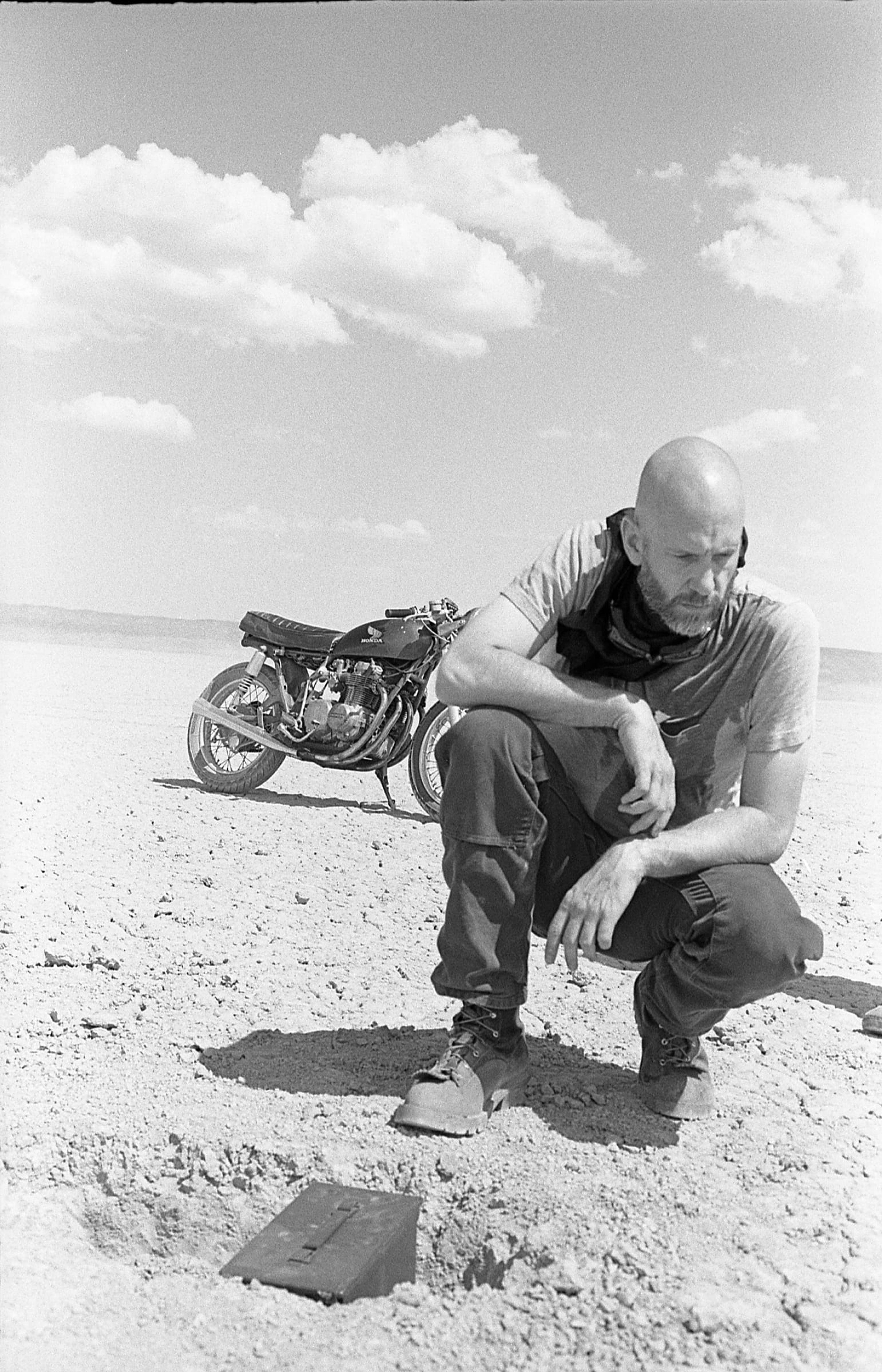 Man crouching beside a motorcycle on a desert lakebed