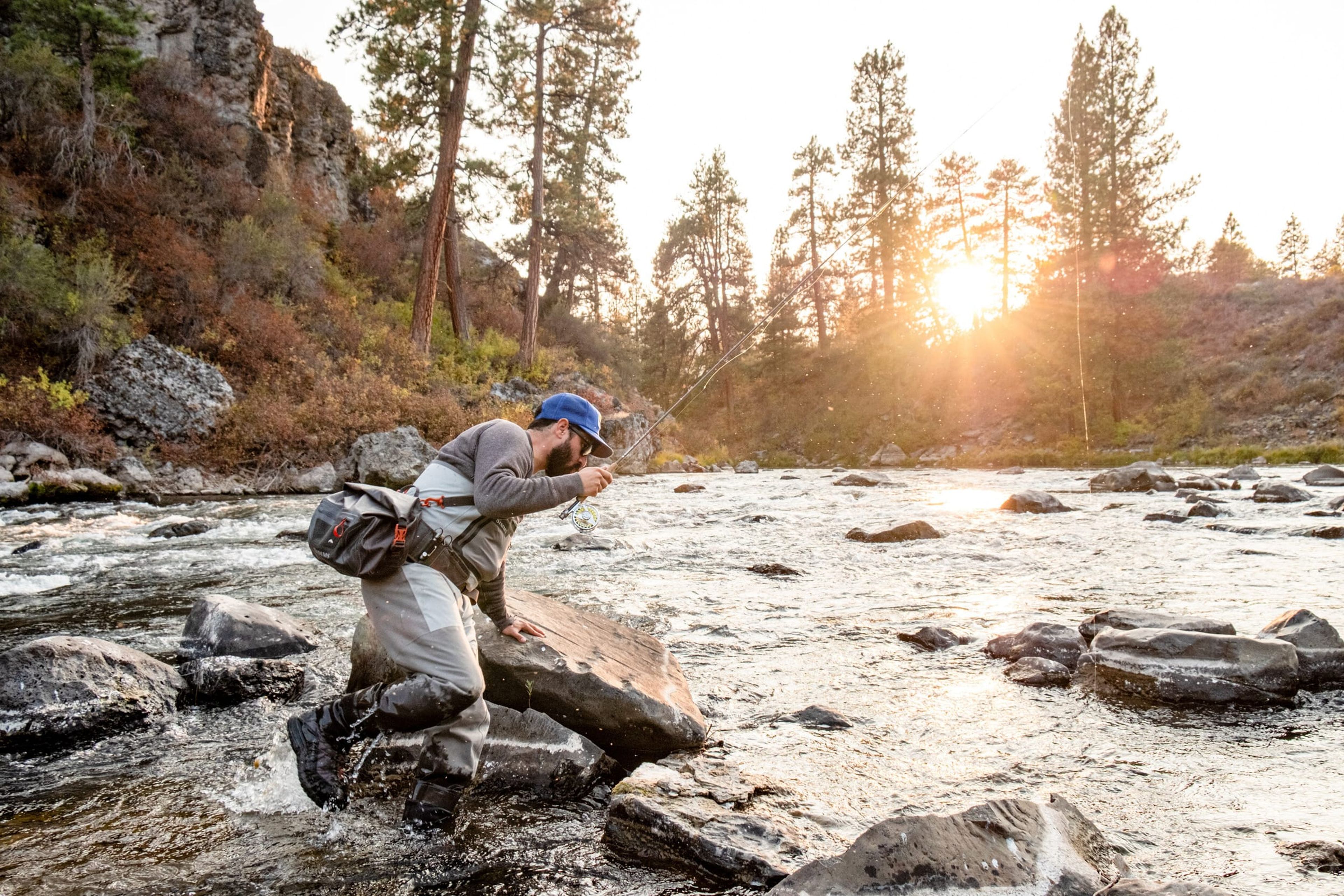 Angler climbing over river boulders at sunset