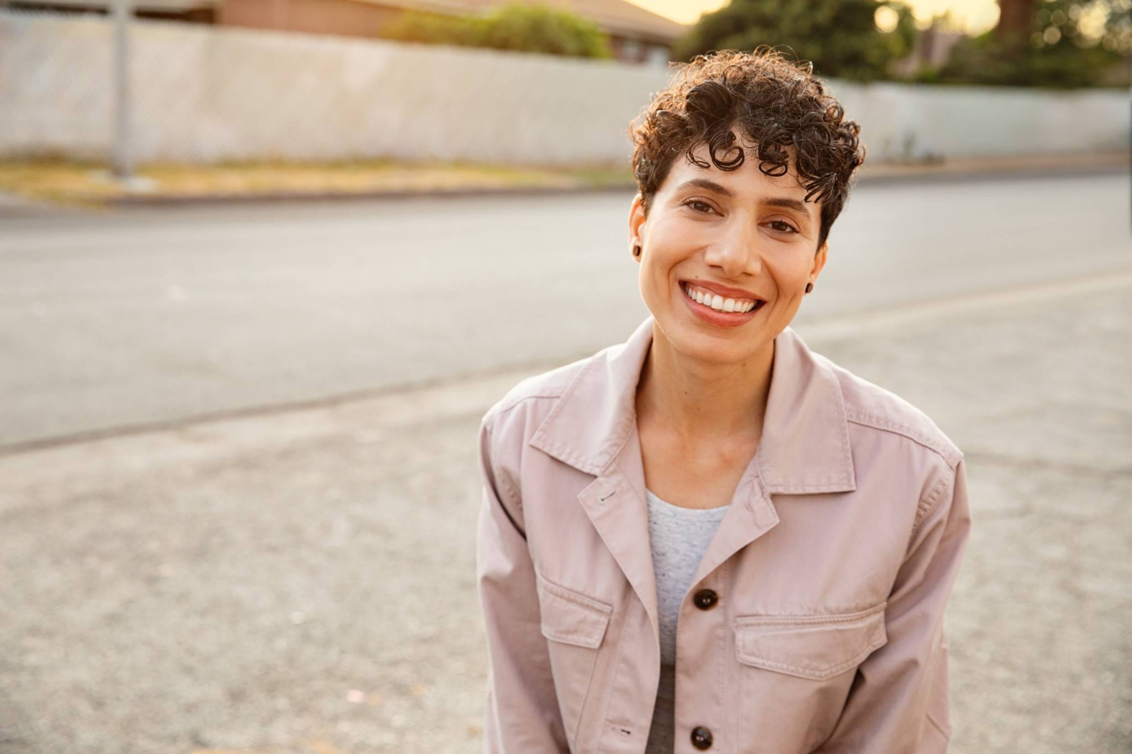 Smiling woman in a pink jacket on a sunlit street