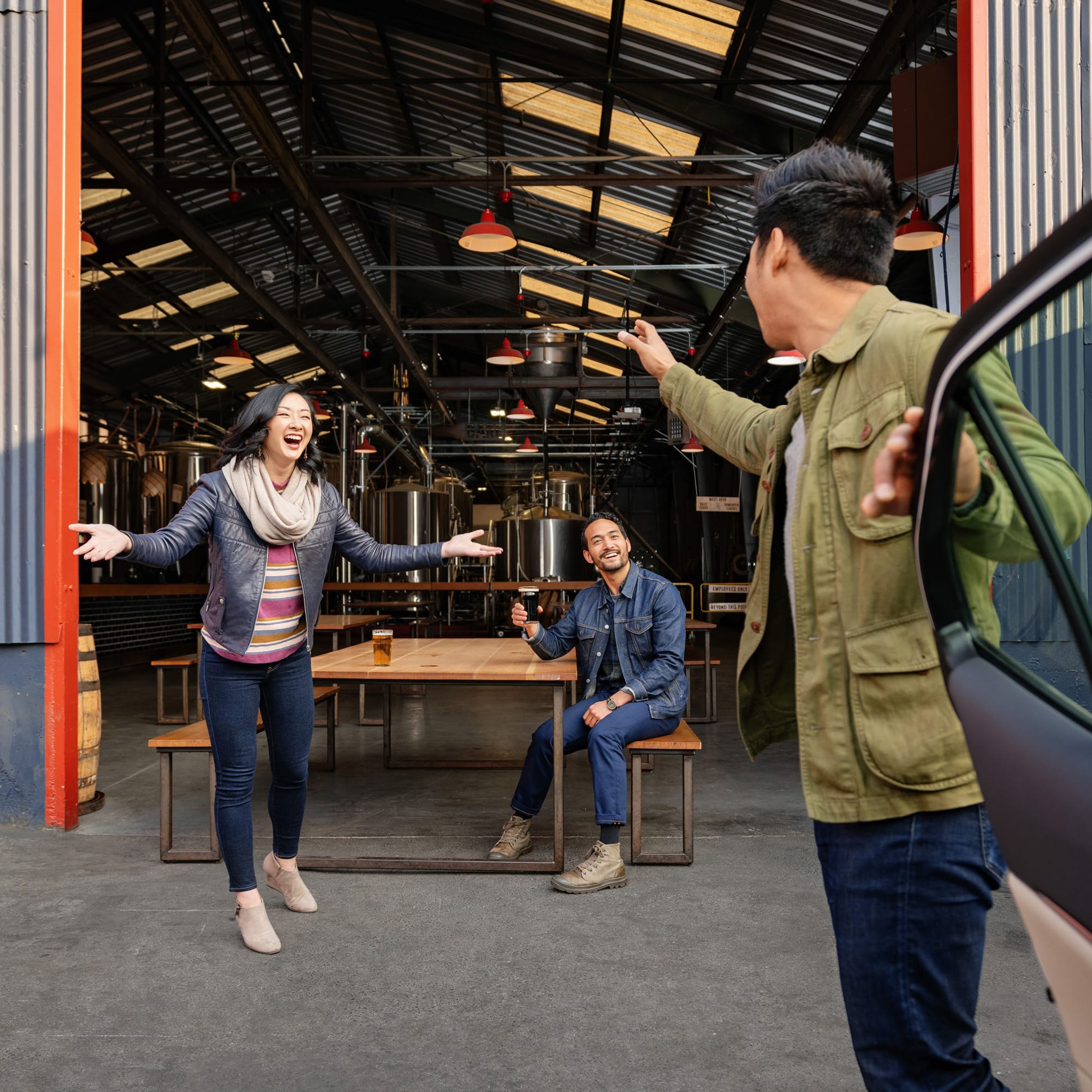 Friends greeting each other at a brewery as one steps out of a car
