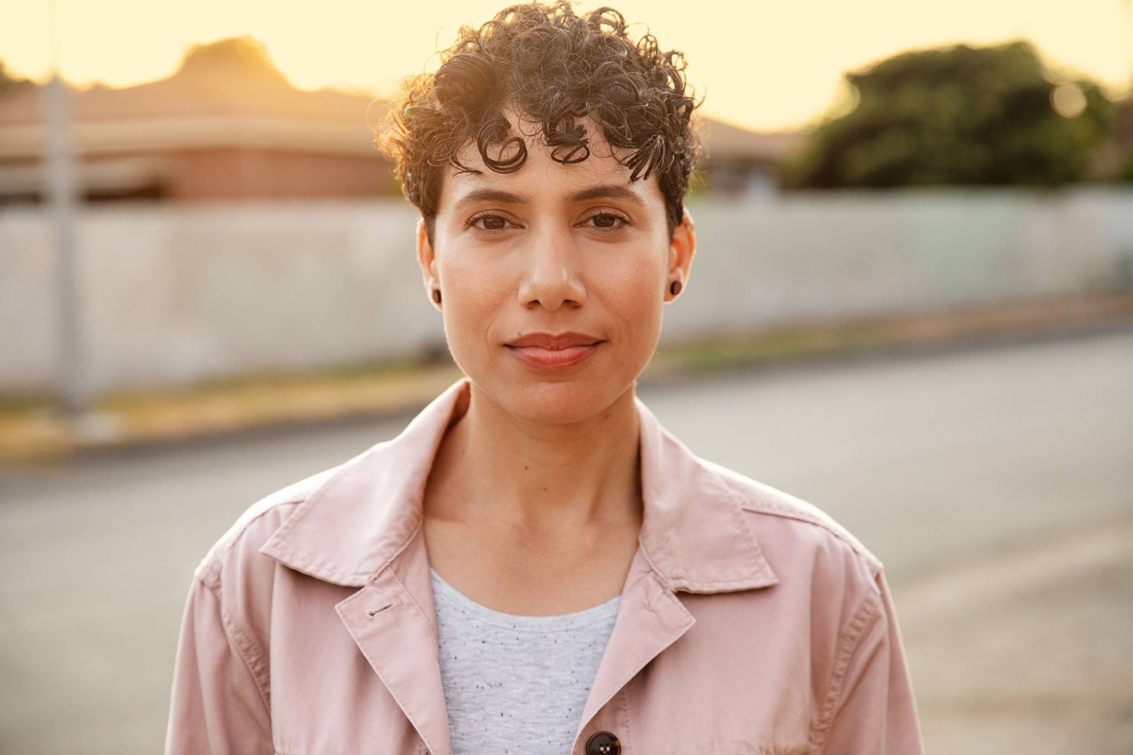 Woman in a pink jacket at golden hour, looking into the camera
