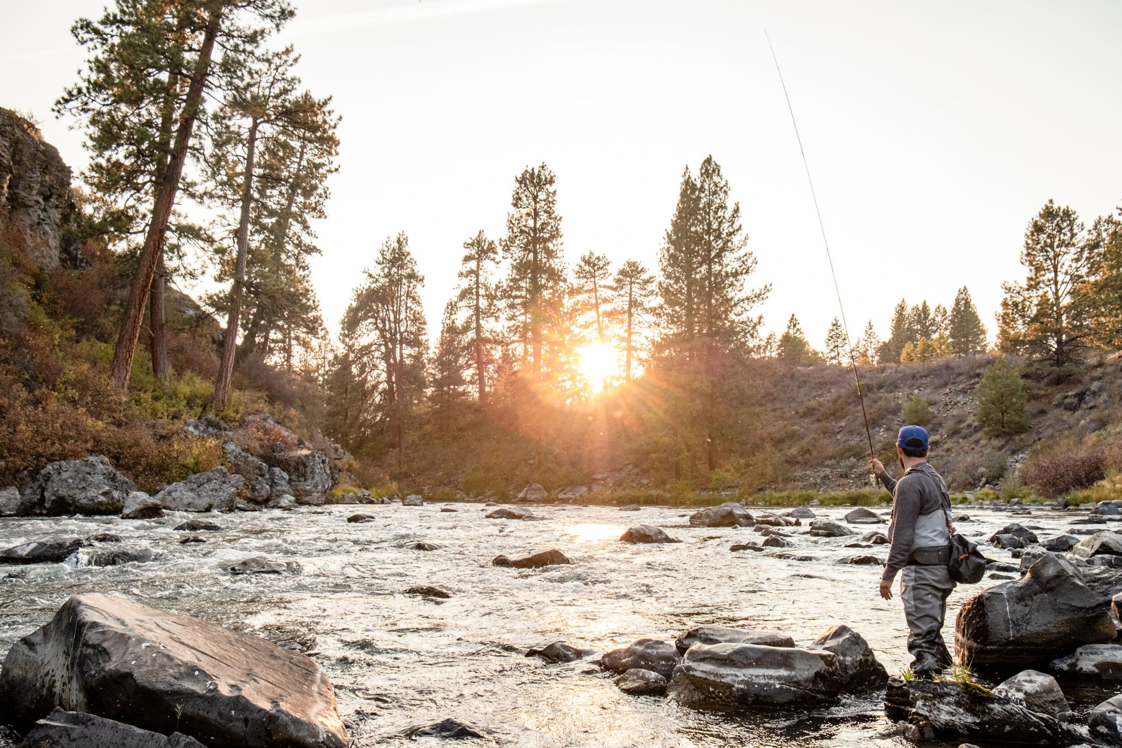 Angler casting on a rocky river at sunset