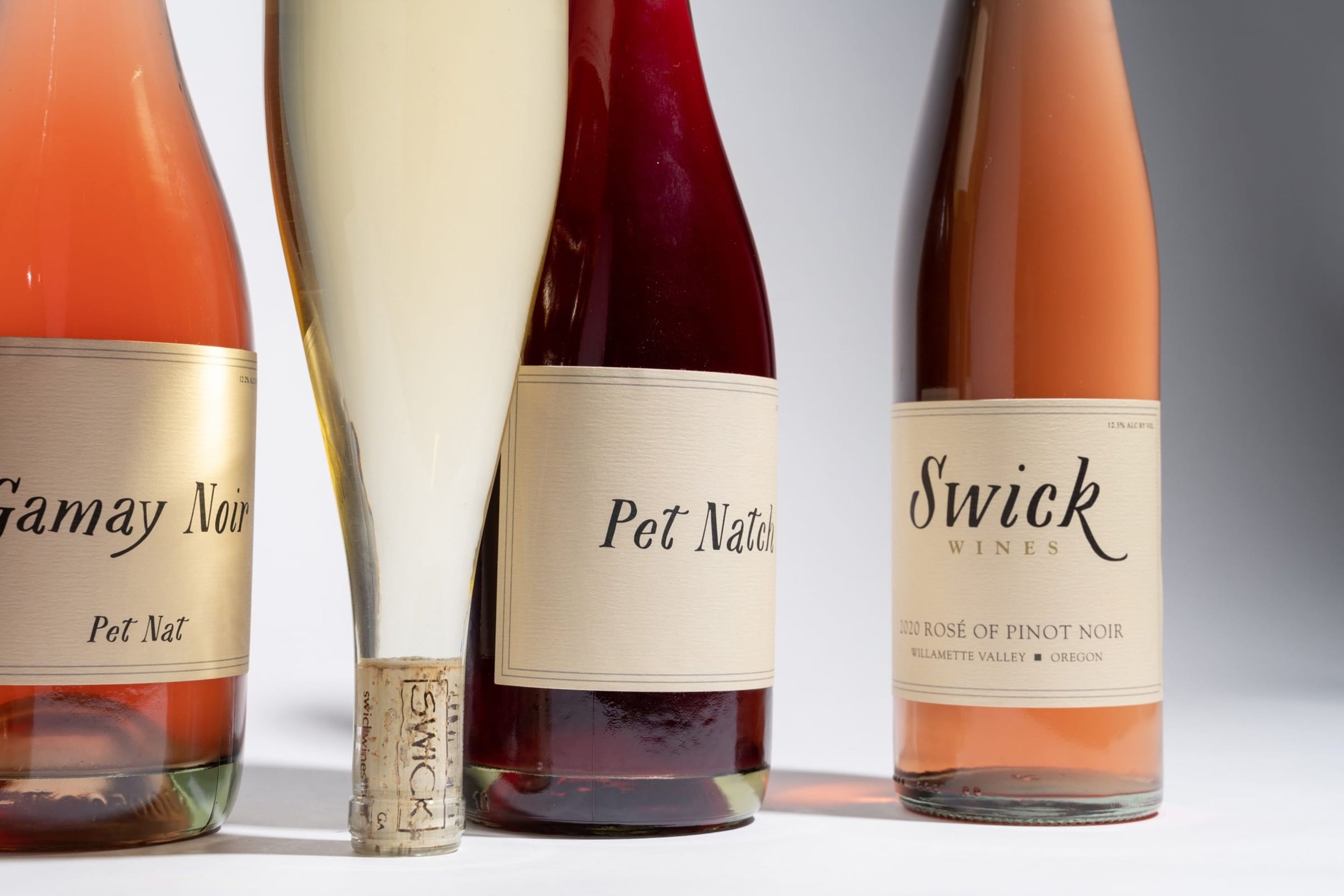 Swick wine bottles lined up beside a cork