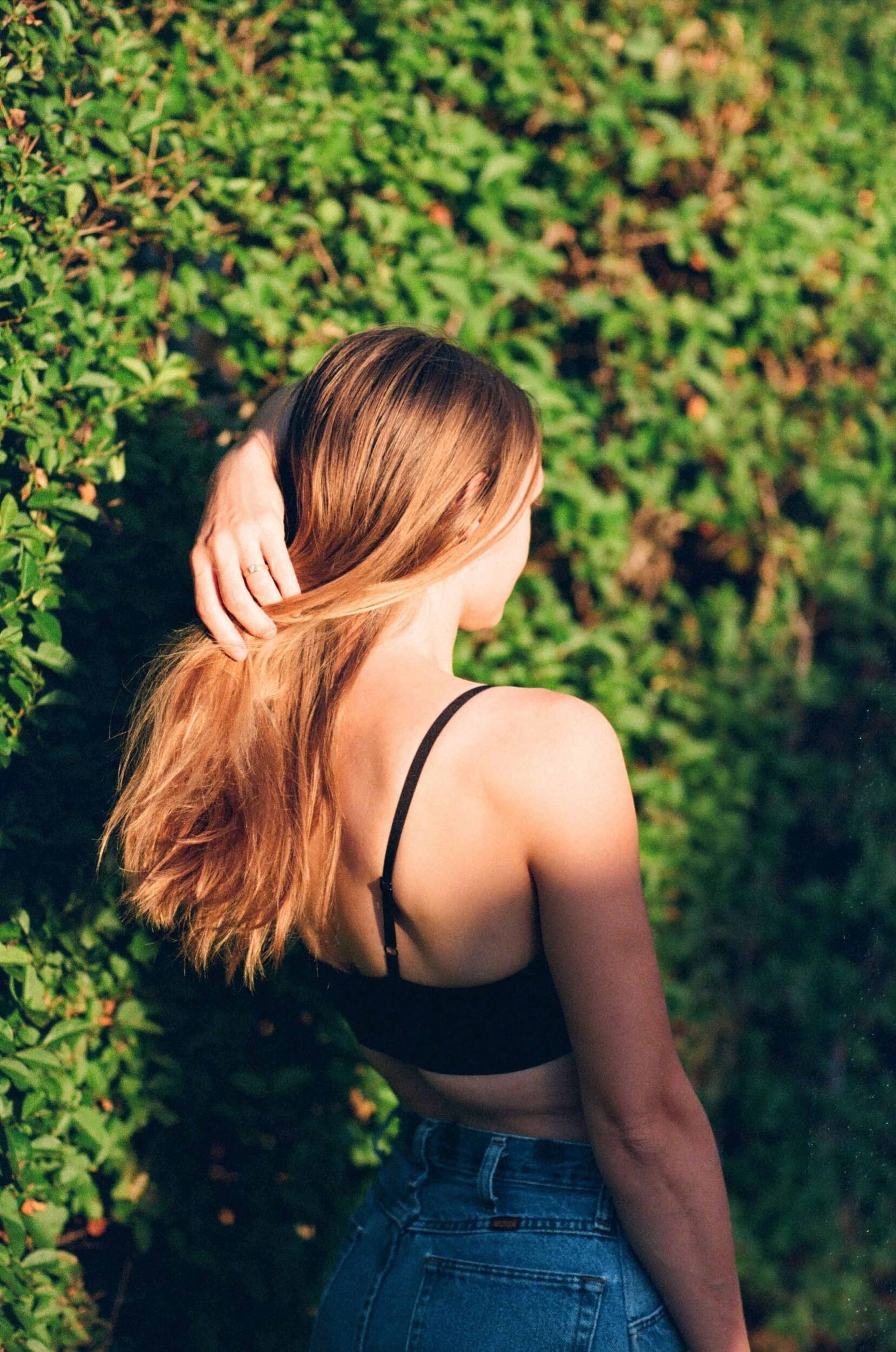 Woman with long hair seen from behind against green leaves