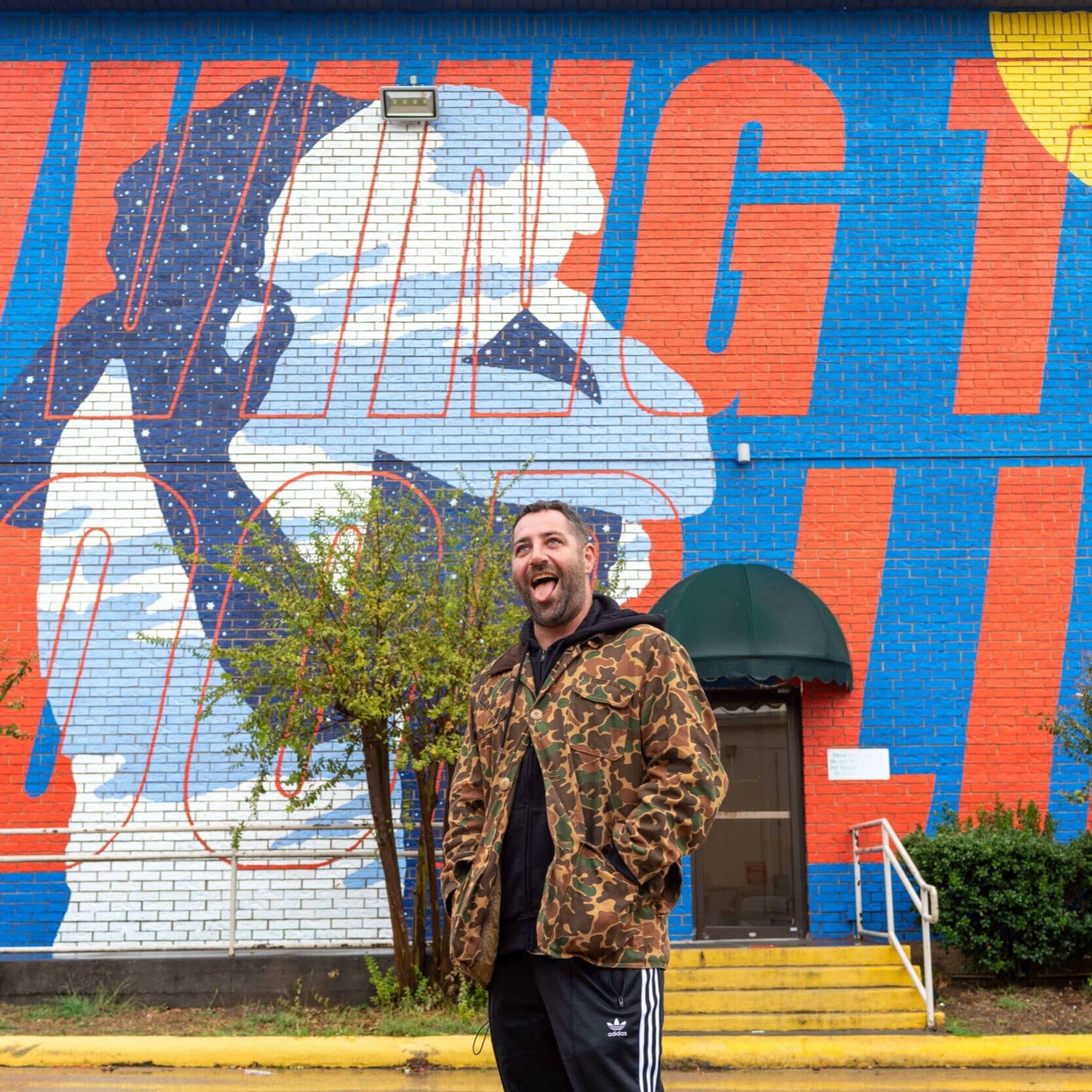Smiling artist in front of the “Living the Good Life” mural