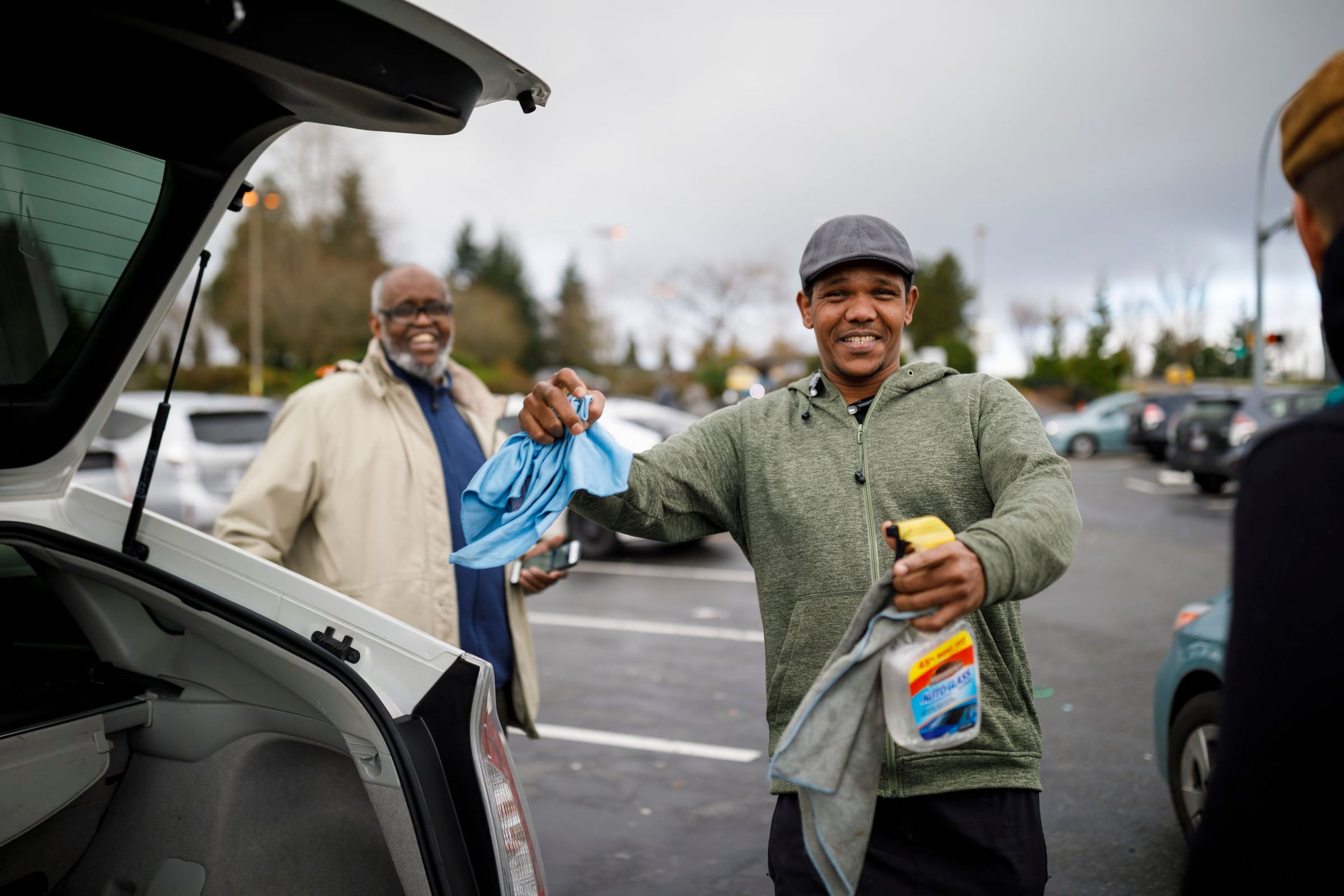 Two men laughing beside an open car trunk
