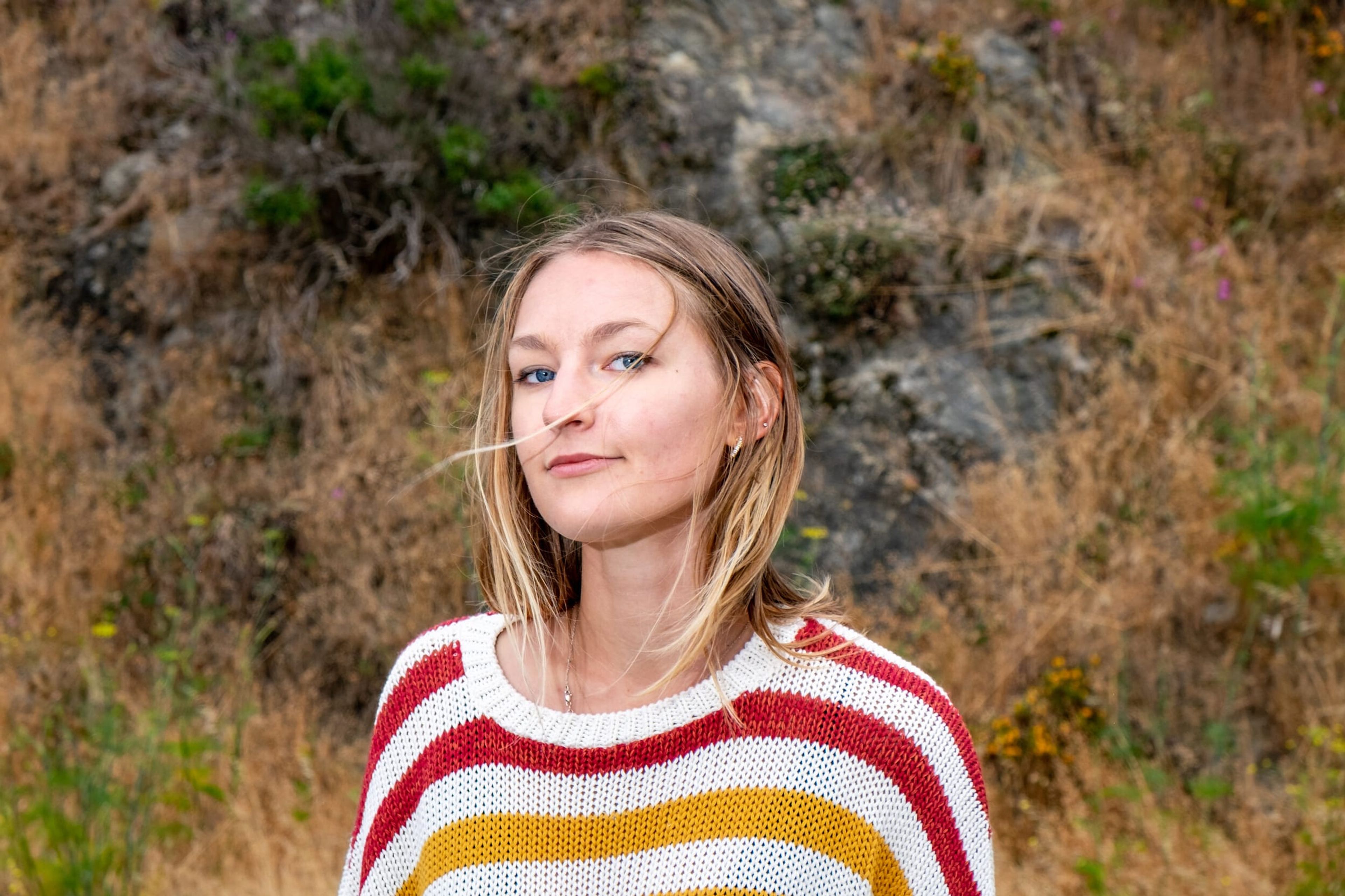 Portrait of Megan in a striped sweater against a grassy hillside