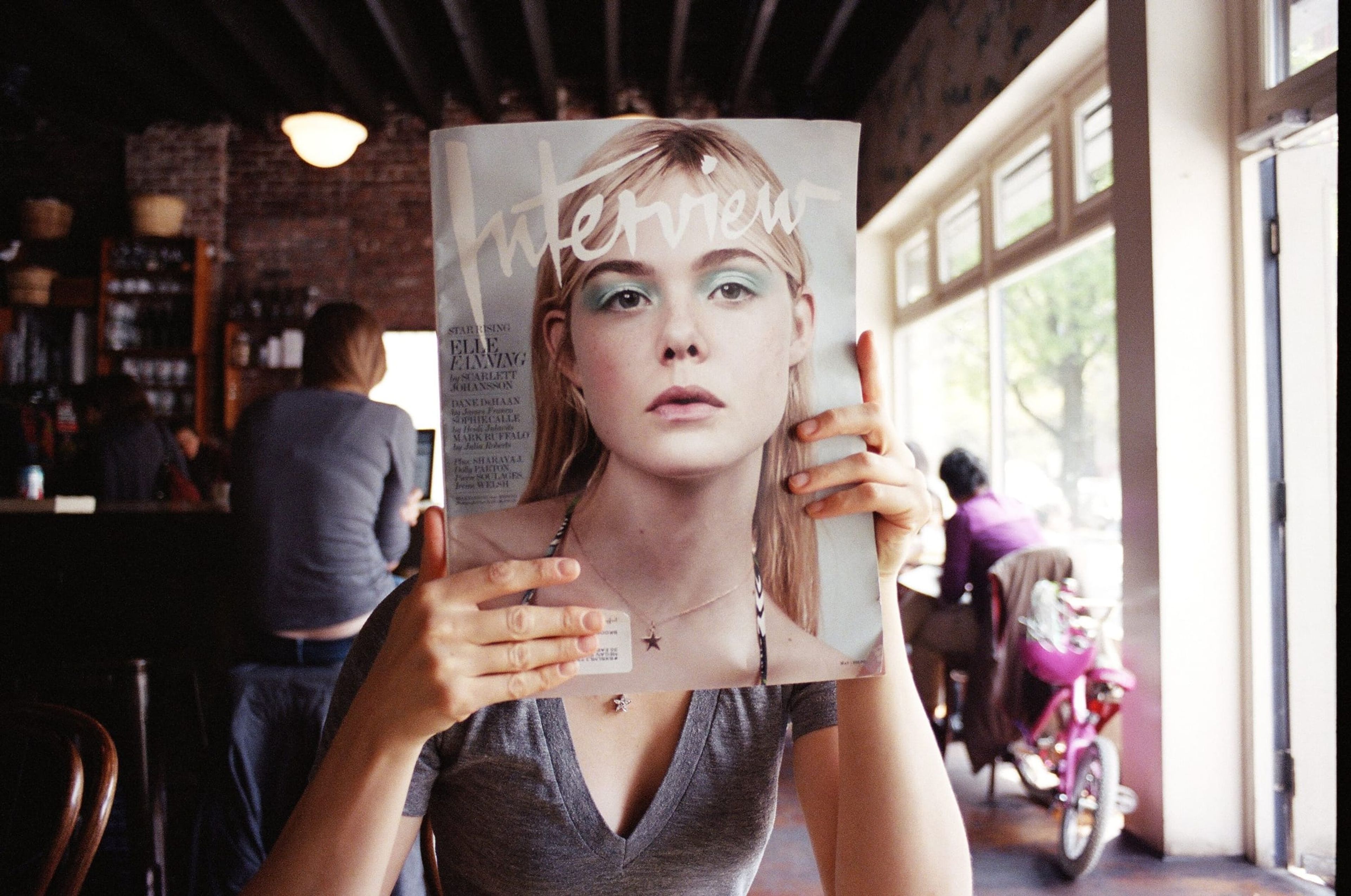 Woman holding an Interview magazine cover in front of her face in a café