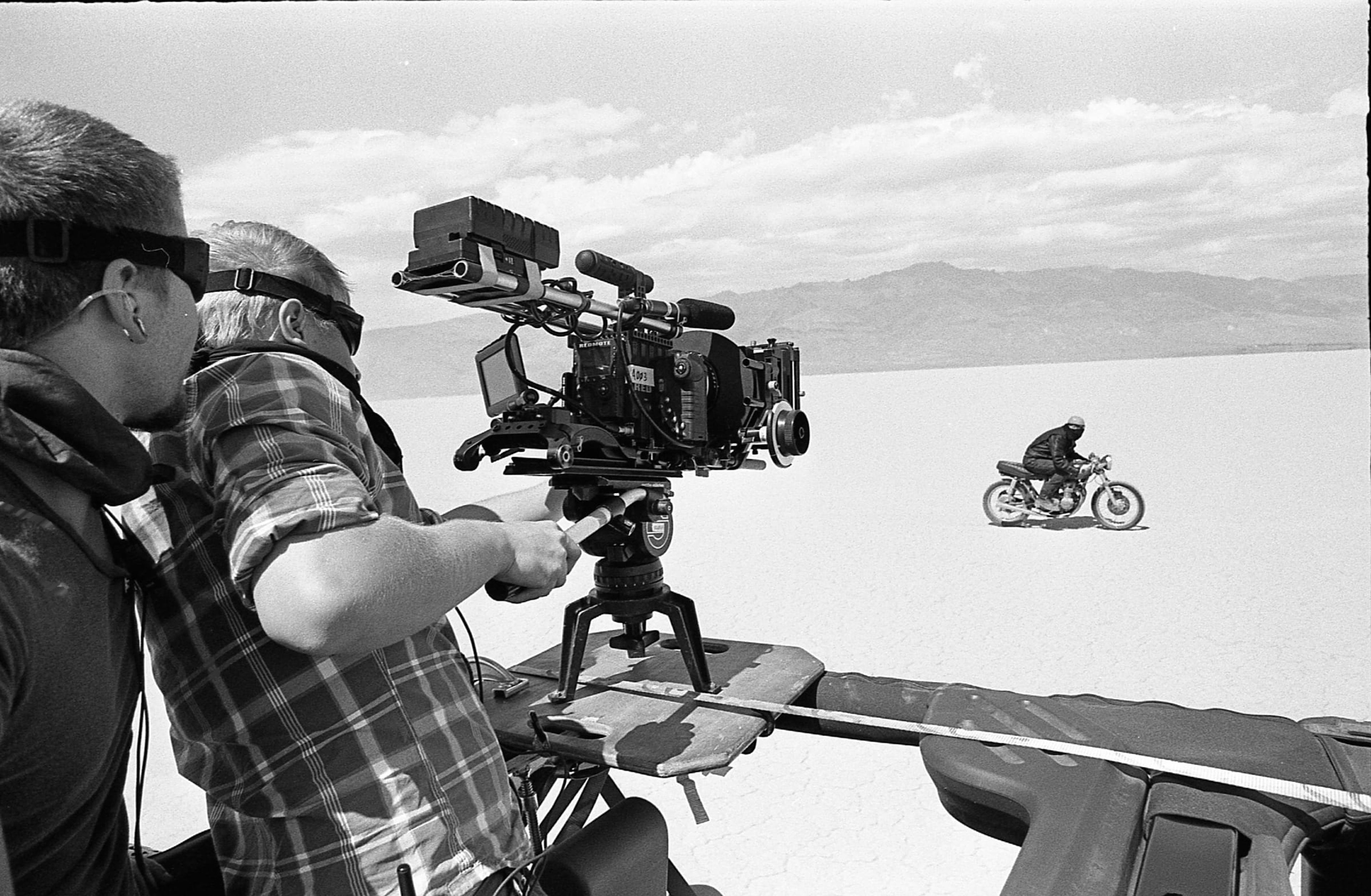 Camera crew filming a motorcyclist on a desert lakebed from a vehicle rig