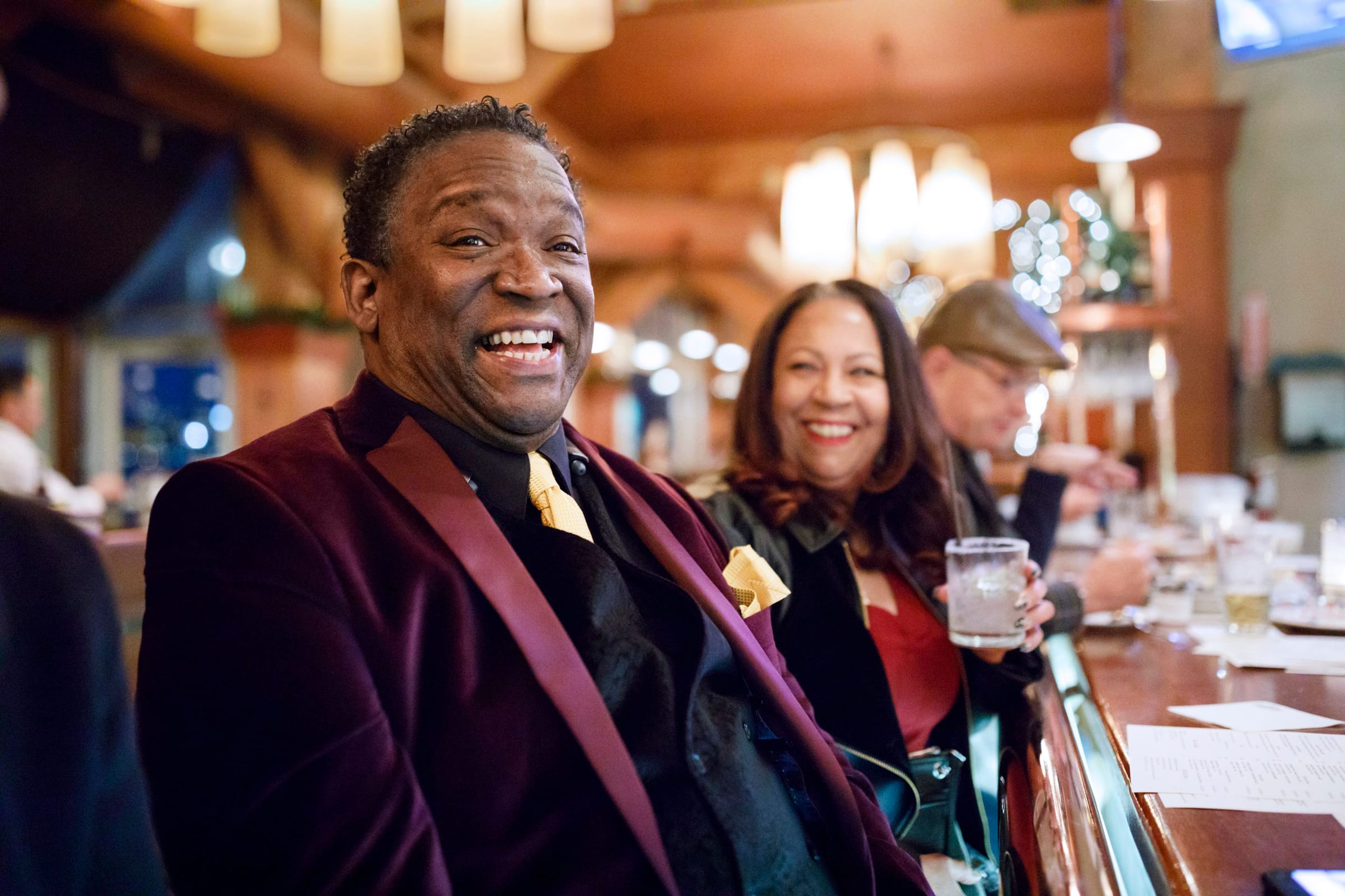 Smiling man in a velvet jacket at a bar with friends