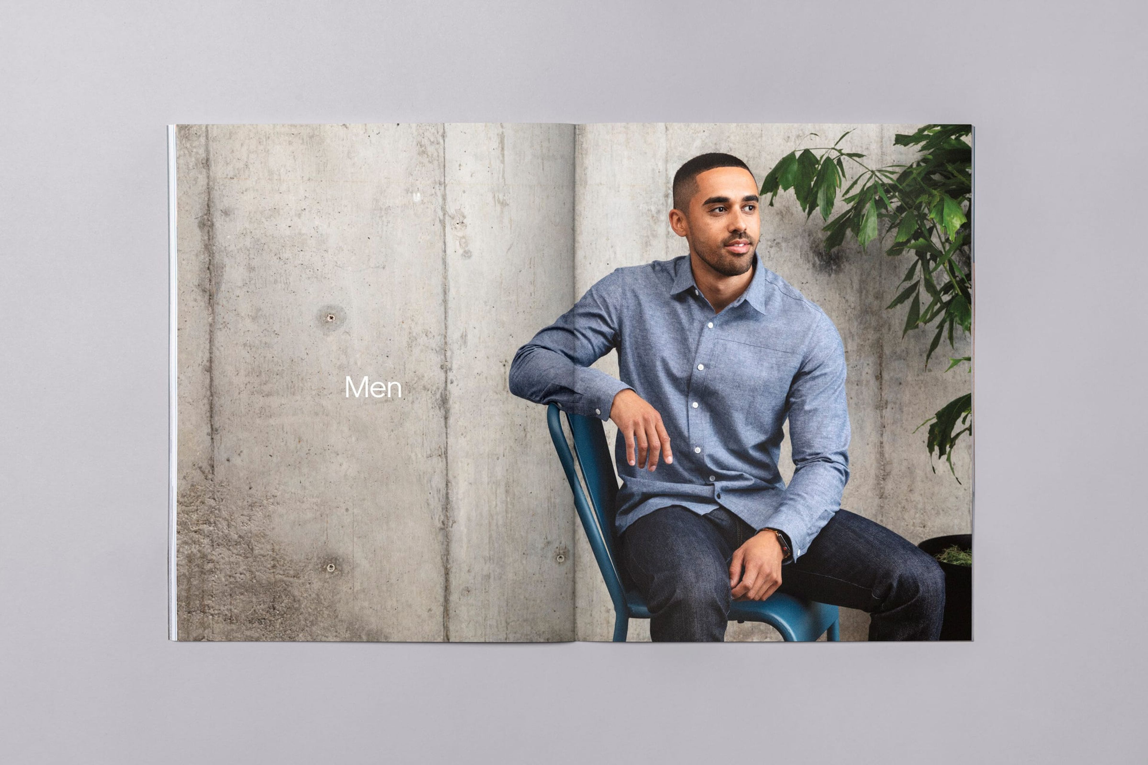 Lookbook “Men” spread: man in a chambray shirt seated against concrete