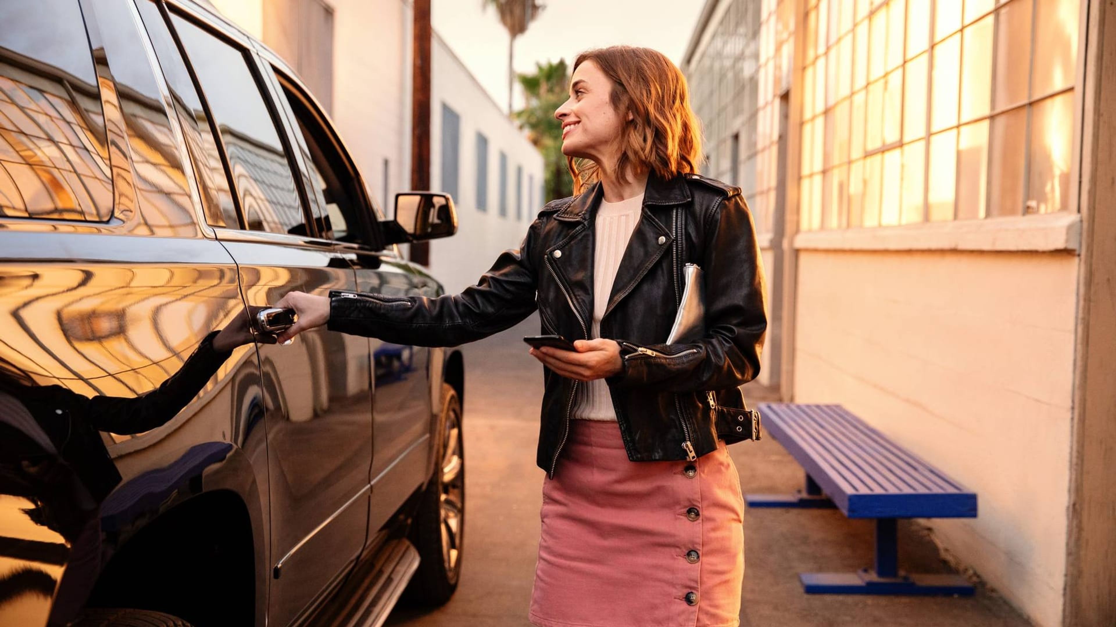 Woman opening the door of a black car in a sunlit alley