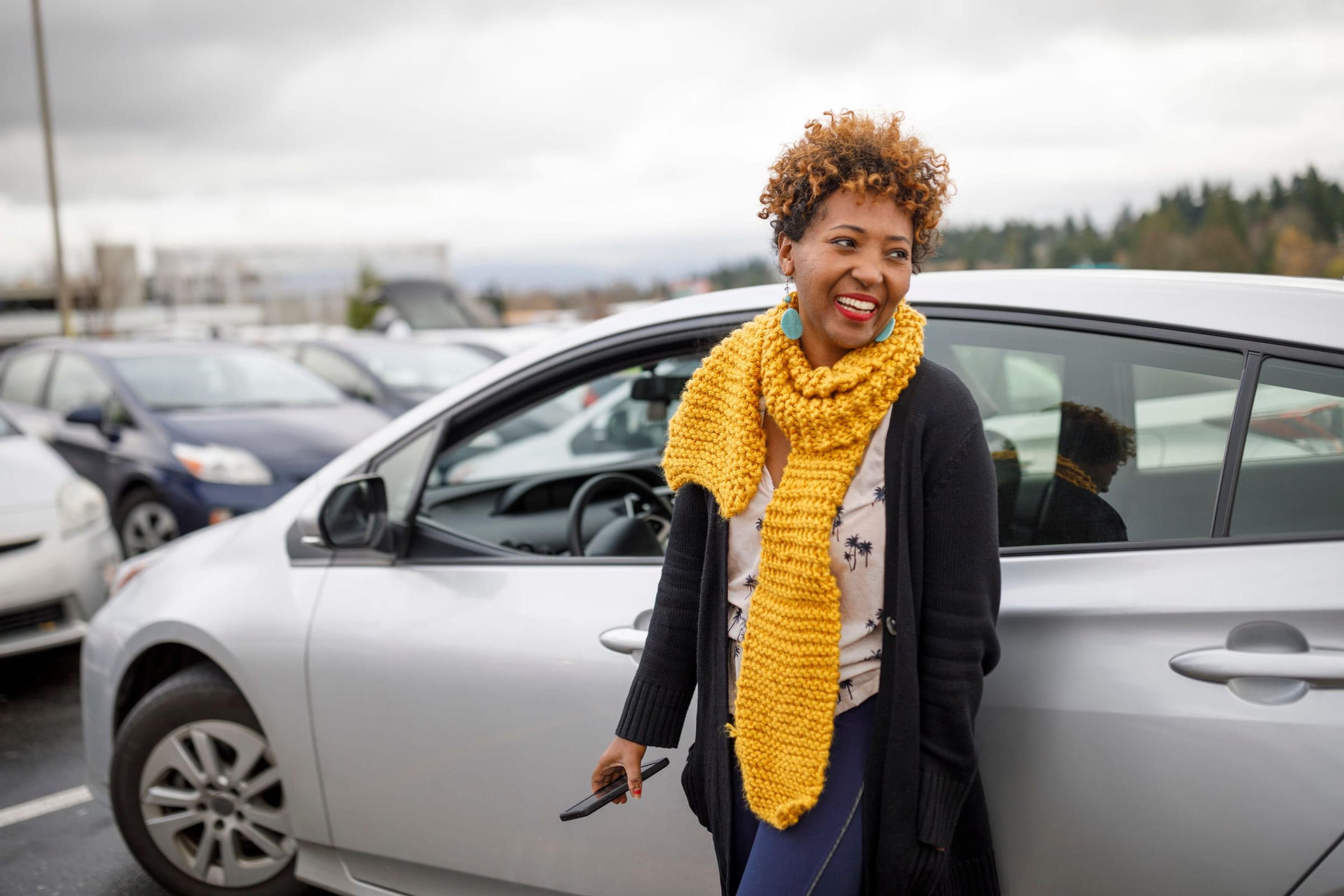 Woman in a yellow scarf beside her silver car