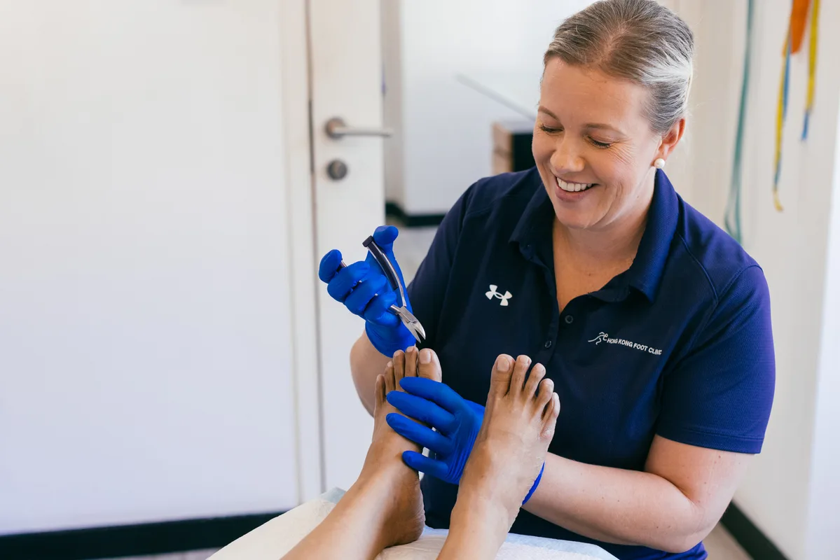 a woman wearing an under armour shirt is holding a pair of scissors over a patient 's foot