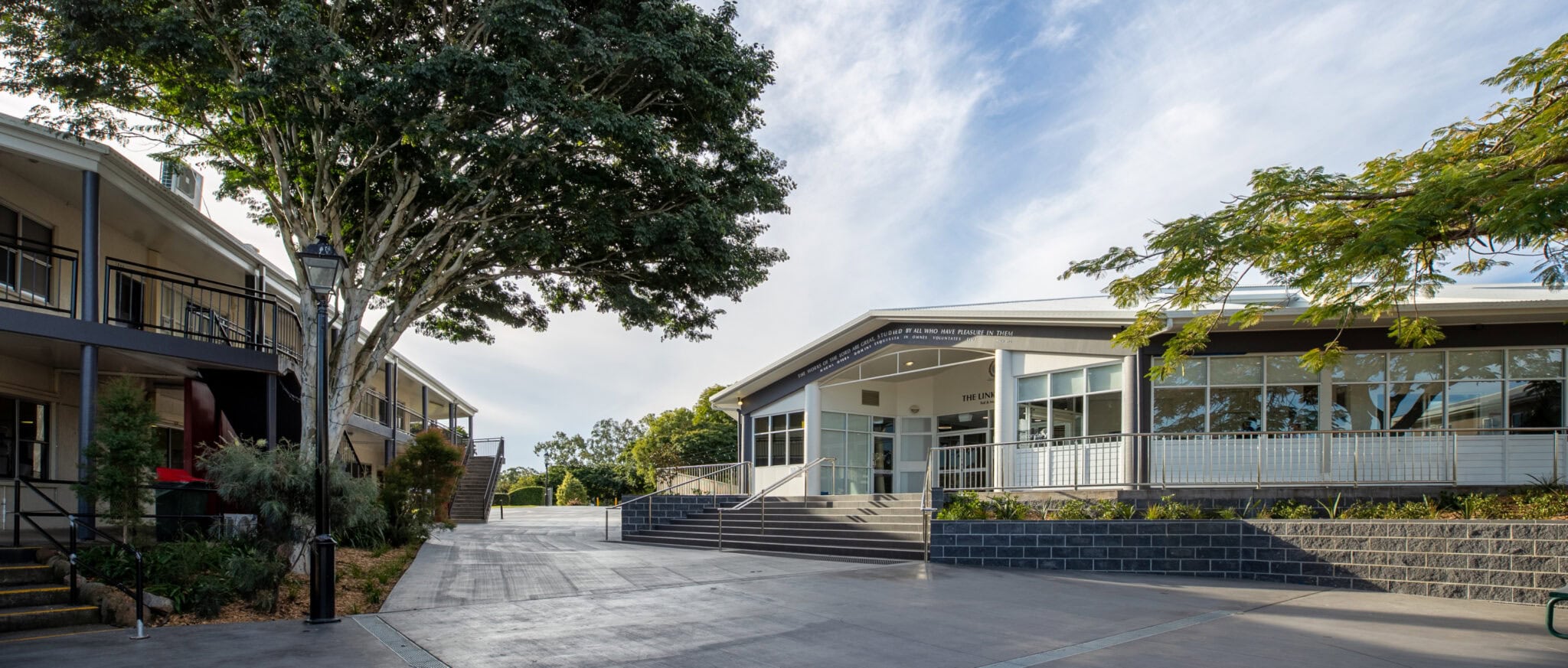 Exterior view of a modern school campus with white buildings, paved pathways, and mature trees.