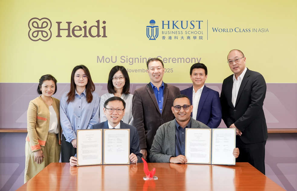 Group photo of eight individuals from Heidi and HKUST Business School at an MoU signing ceremony, with two seated holding signed documents.