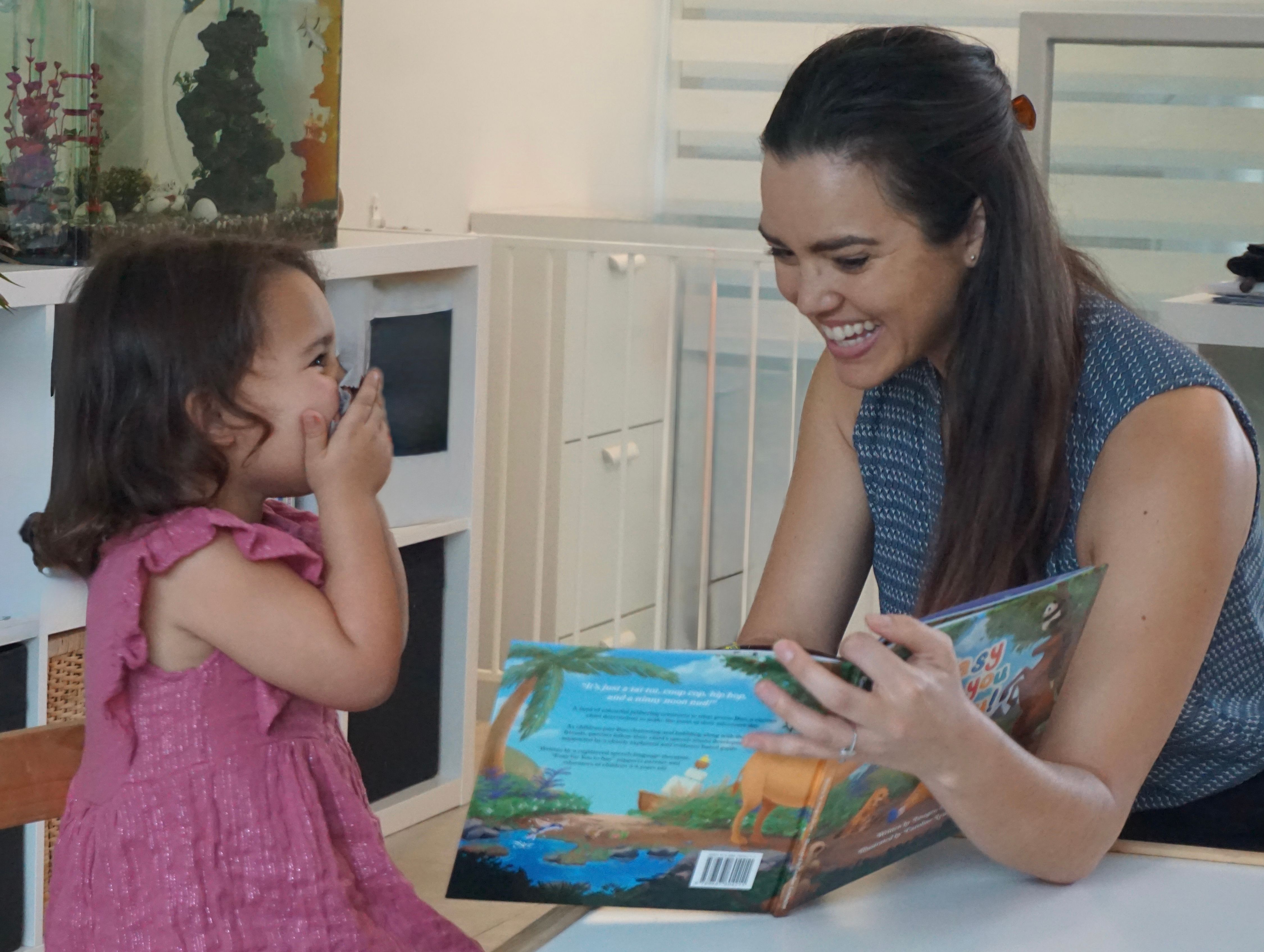 An adult and child laugh excitedly while reading a picture book.