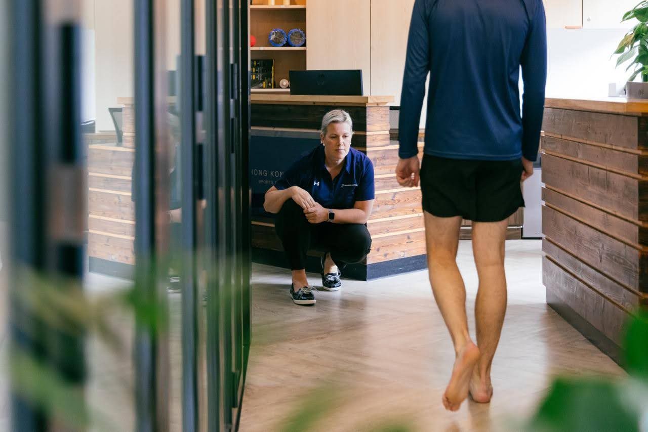 a man is walking barefoot in a hallway while a woman squats next to him .