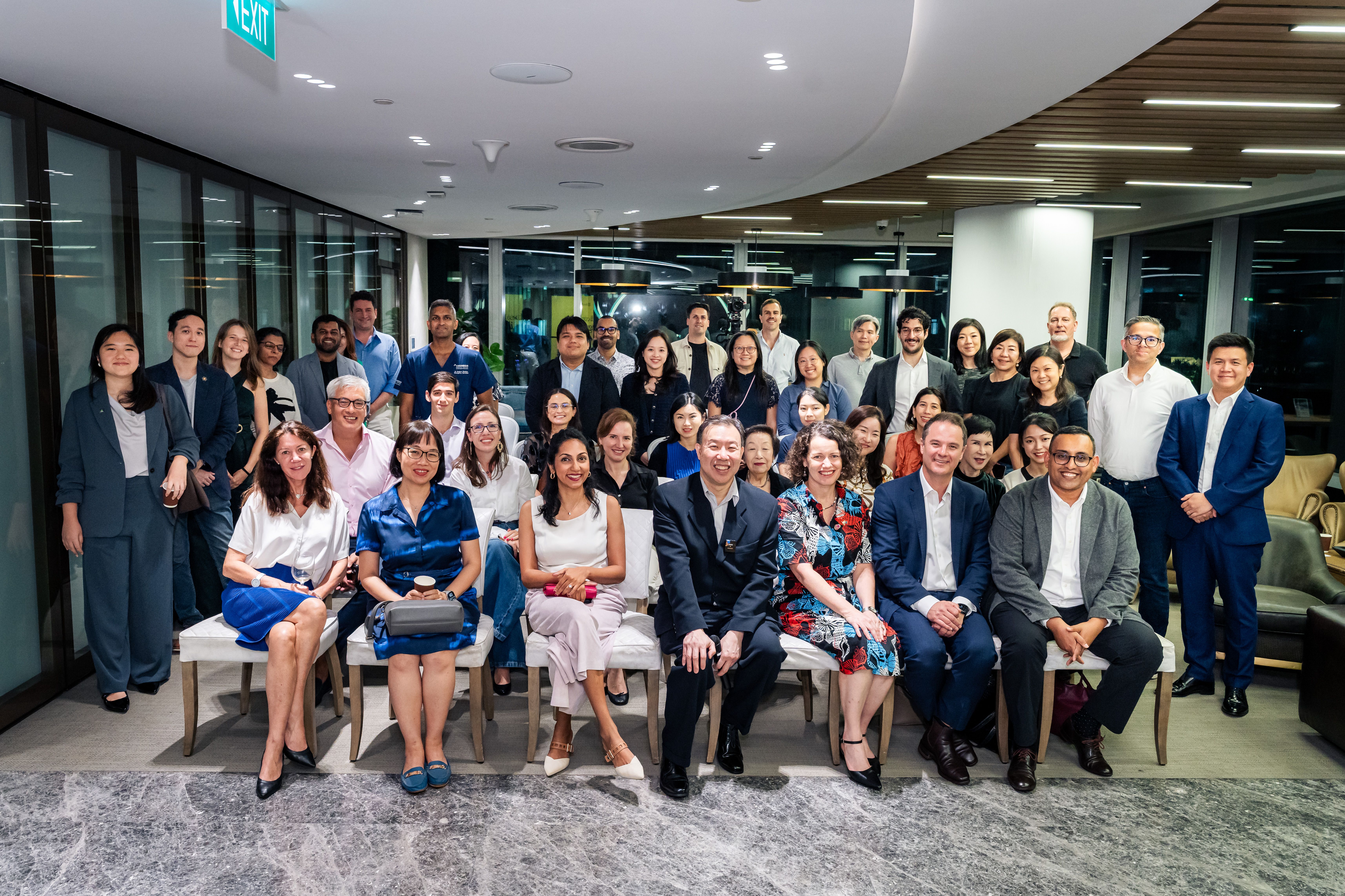 A large, diverse group of smiling professionals poses in a modern office setting.