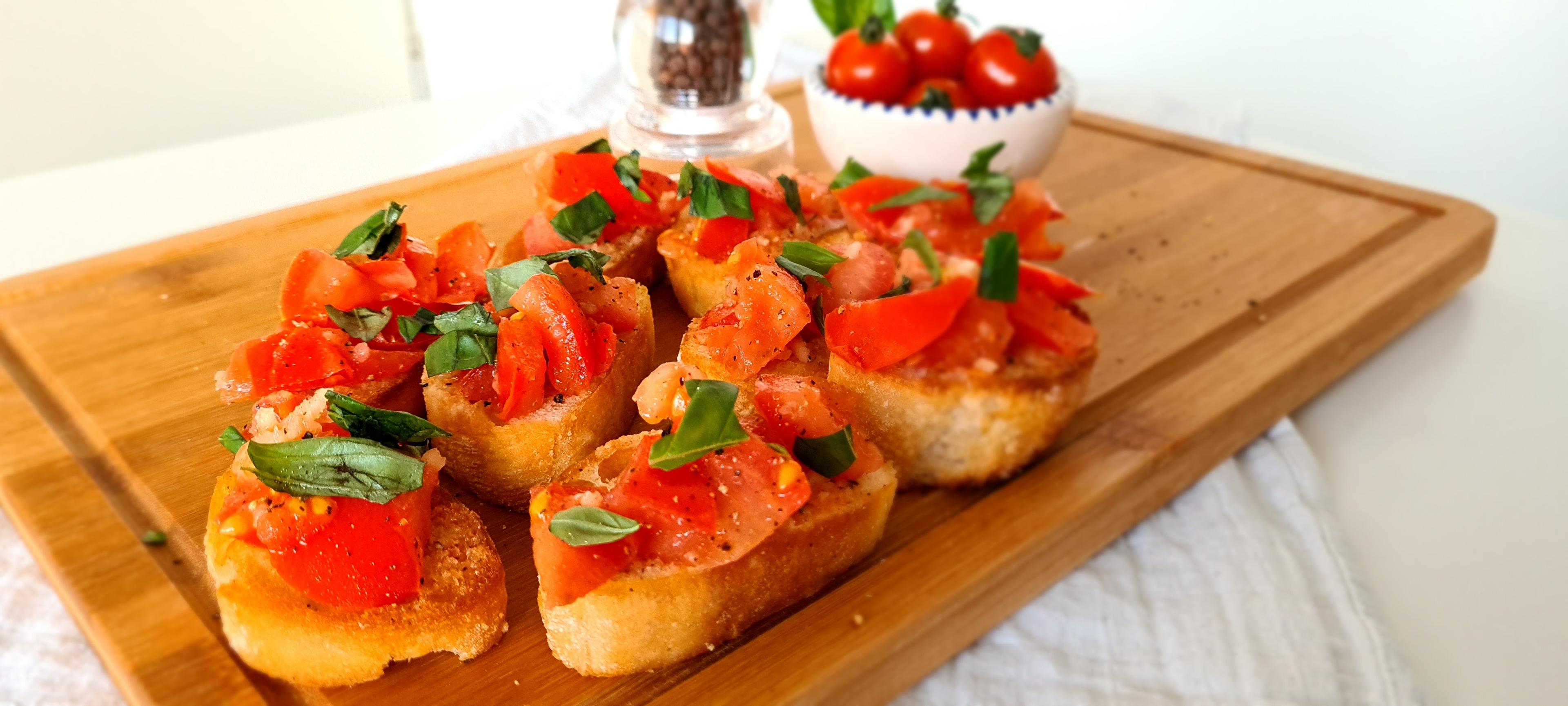 Bruschetta al pomodoro (met tomaat en basilicum) op een houten serveerplank.