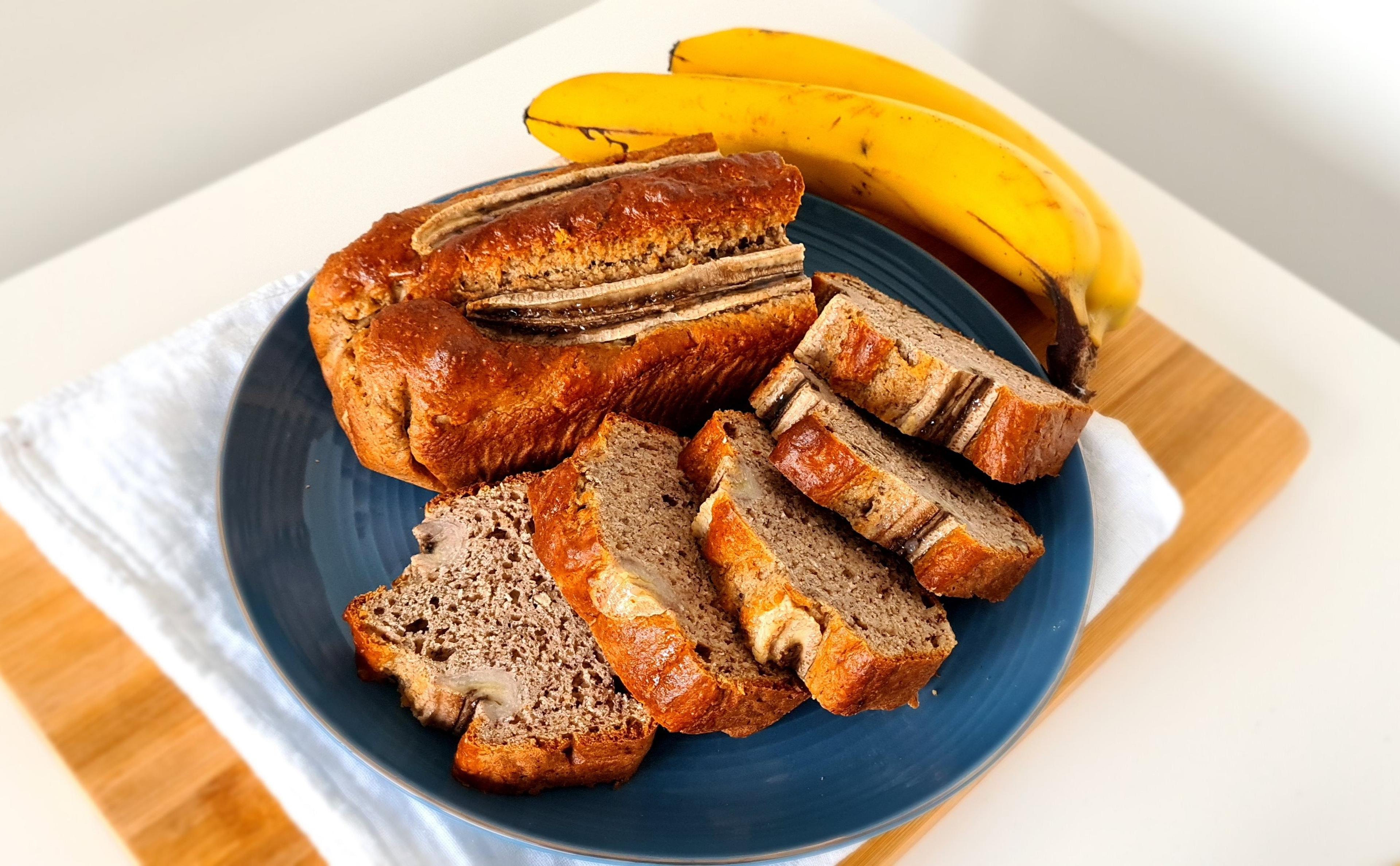 Bananenbrood in plakjes op een blauw bord naast een tros bananen.