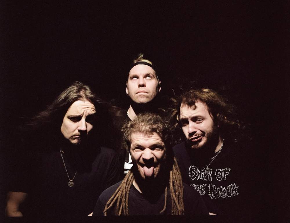 Bandfoto, bei dem nur die in einer Raute angeordneten Köpfe der Mitglieder zu sehen. Alle schneiden eine andere Grimasse.
