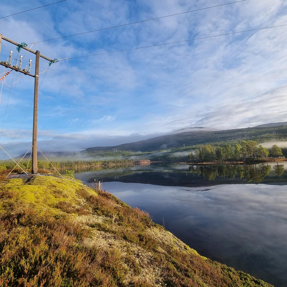 Montør som jobber i stolpe med vakker natur rundt seg.