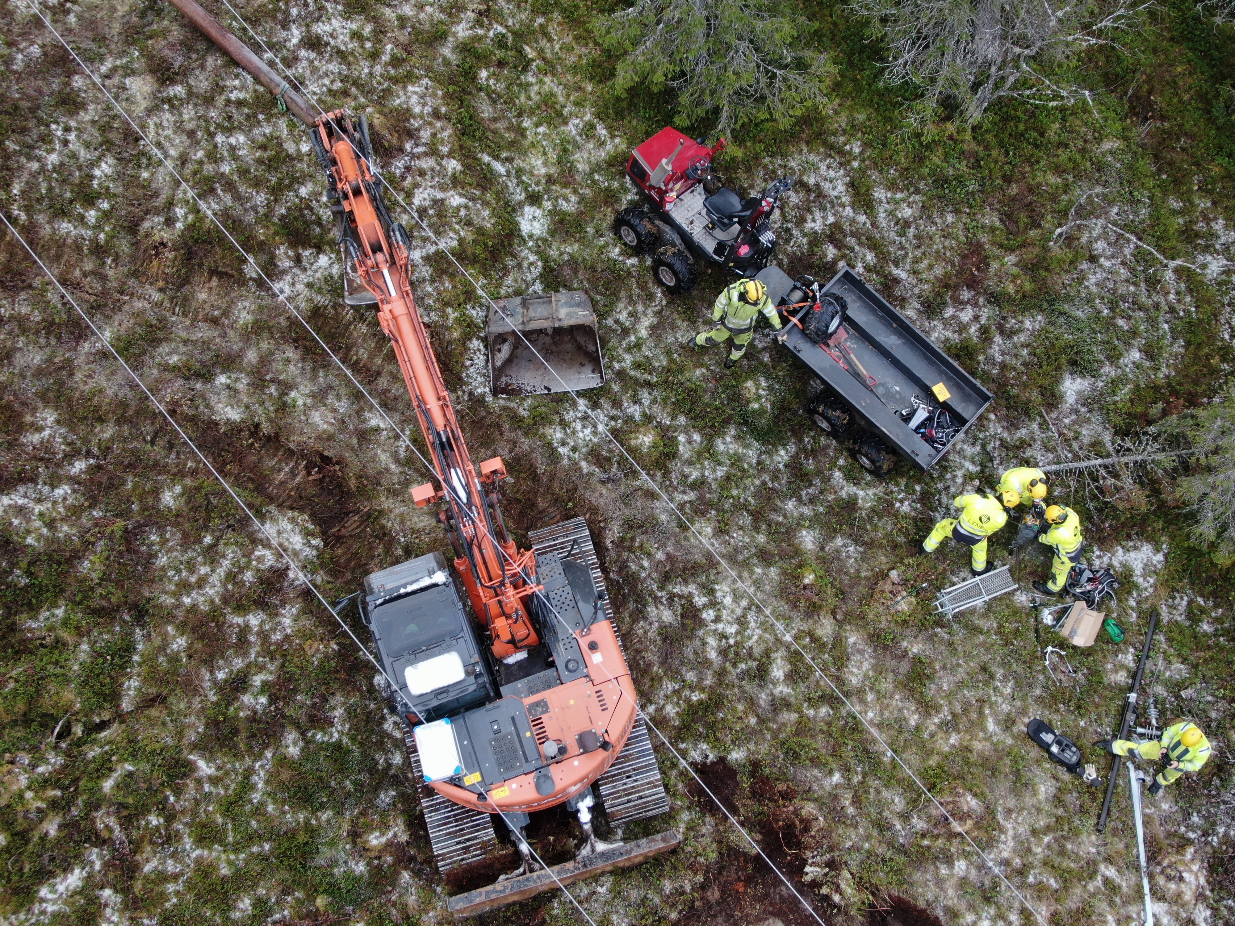 Dronebilde av høyspentlinje. Med montører og gravemaskin under.