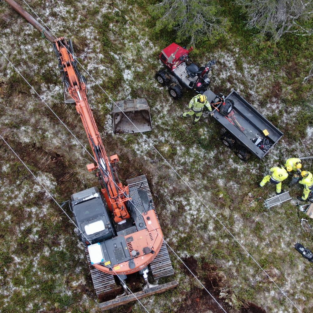 Dronebilde av høyspentlinje. Med montører og gravemaskin under.