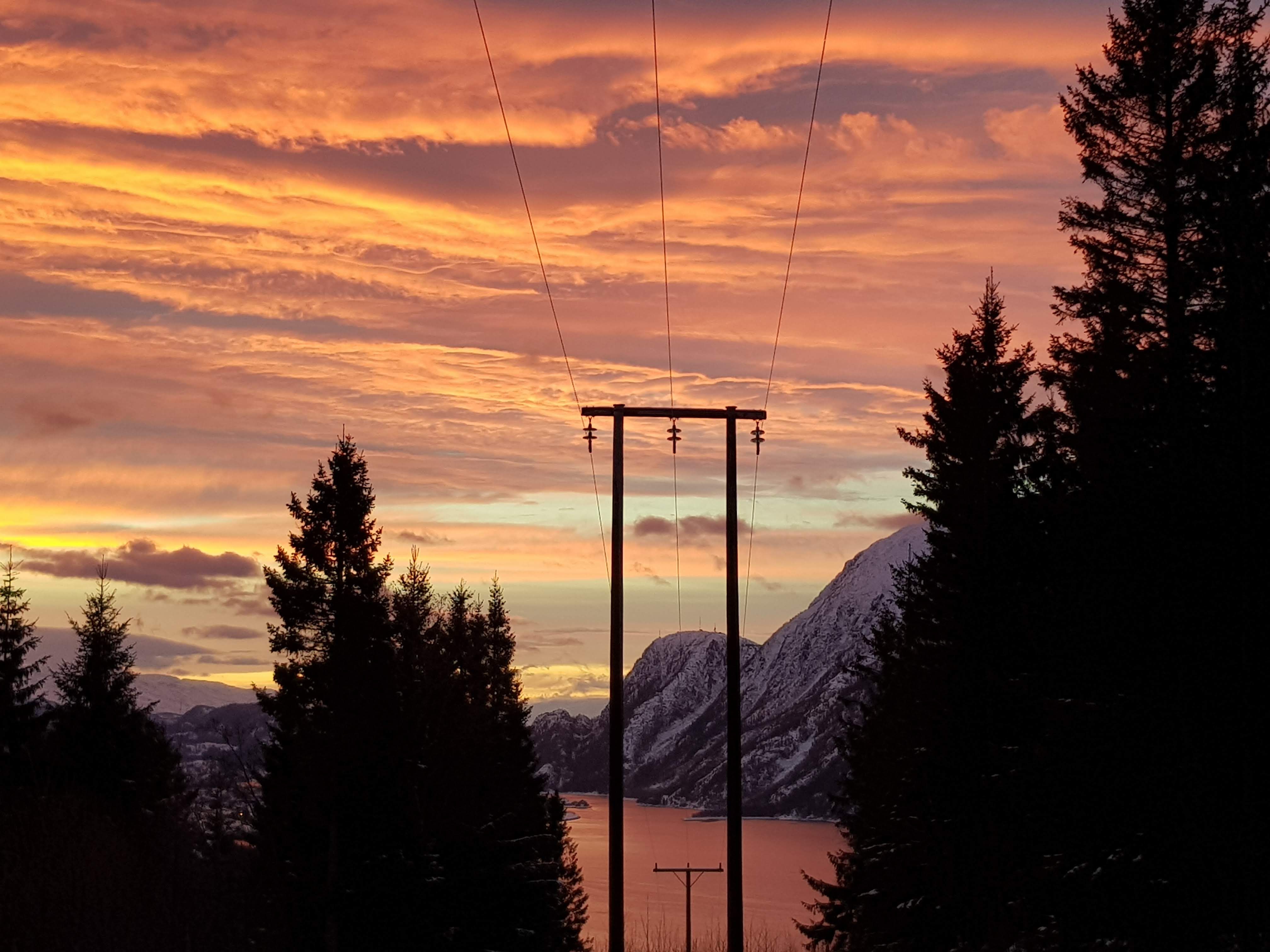 Linjer og stolpe med vakker, rød himmel og hav.