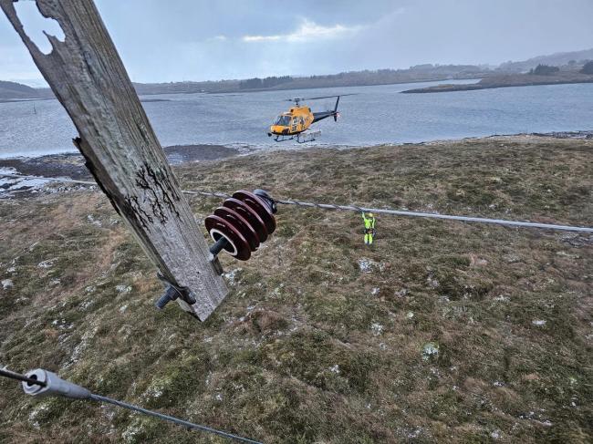 Utsikt fra mast under reperasjon ved kysten. Helikopter og montør i bakgrunn.