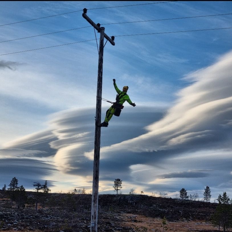 Montør i stolpe med vakker himmel i bakgrunnen.