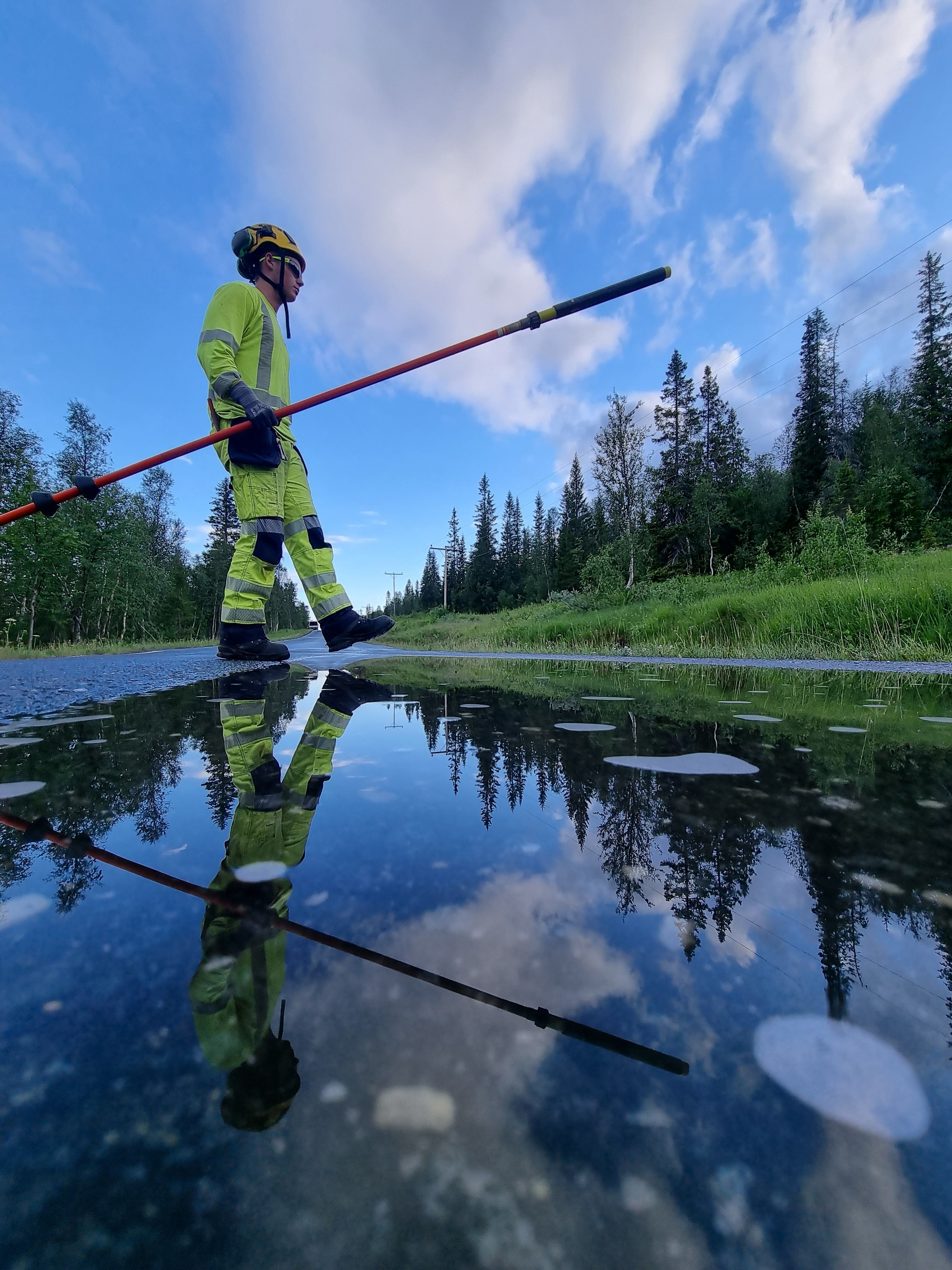 Montør som går over en våt vei. Med skog i bakgrunnen.