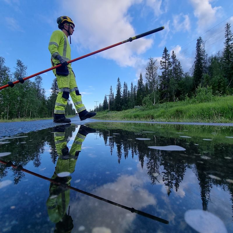 Montør som går over en våt vei. Med skog i bakgrunnen.