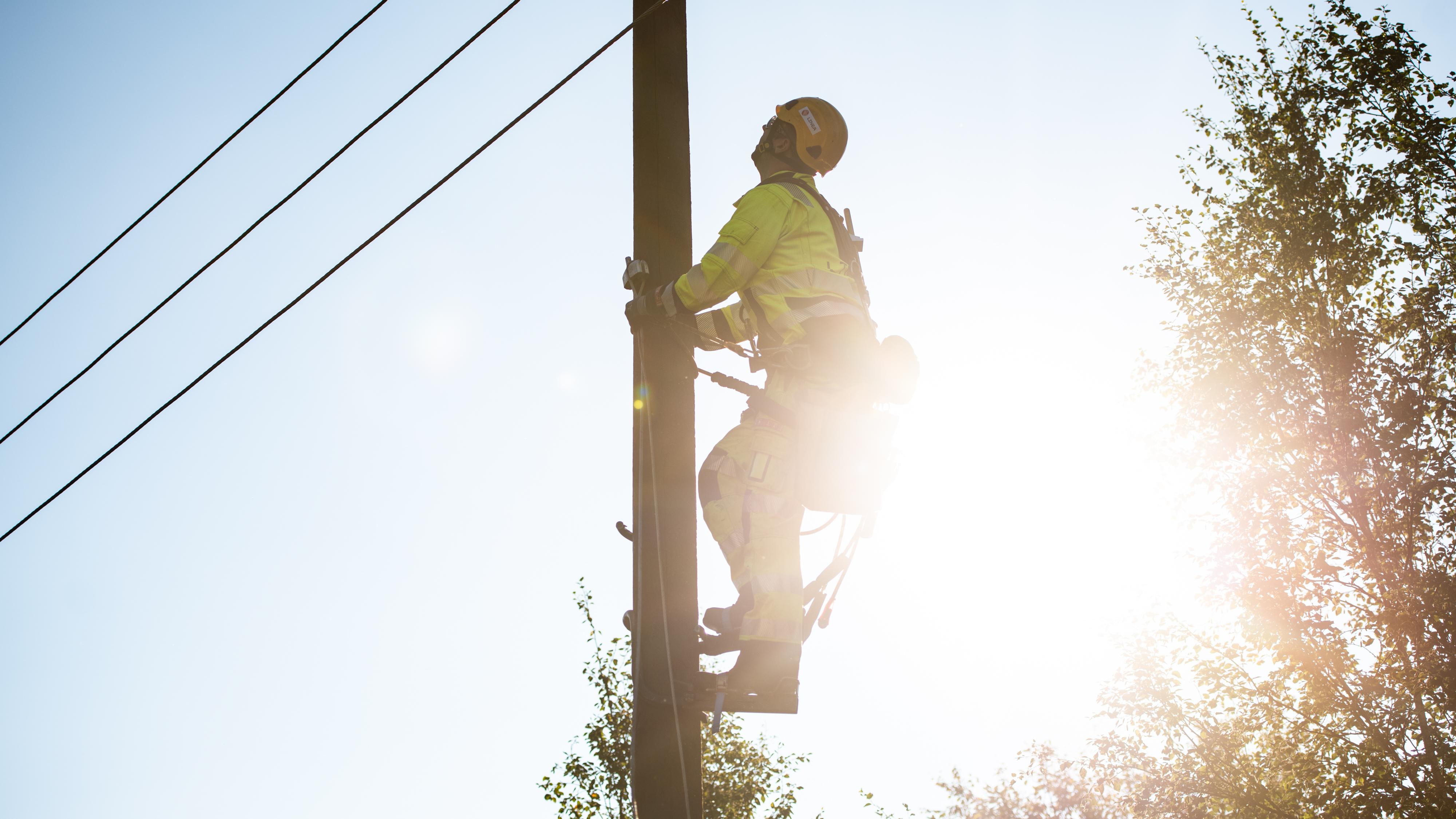 Montør på tur opp i stolpe, med sol i bakgrunnen.