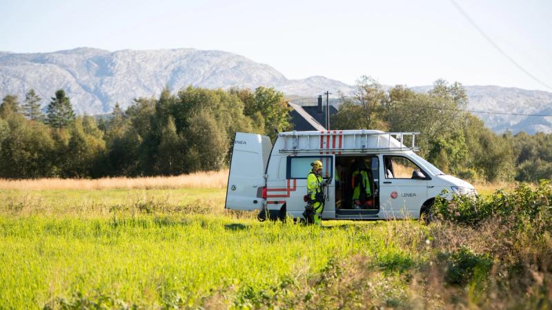 Bil fra Linea og montør som står ute på gresset ved skogen.