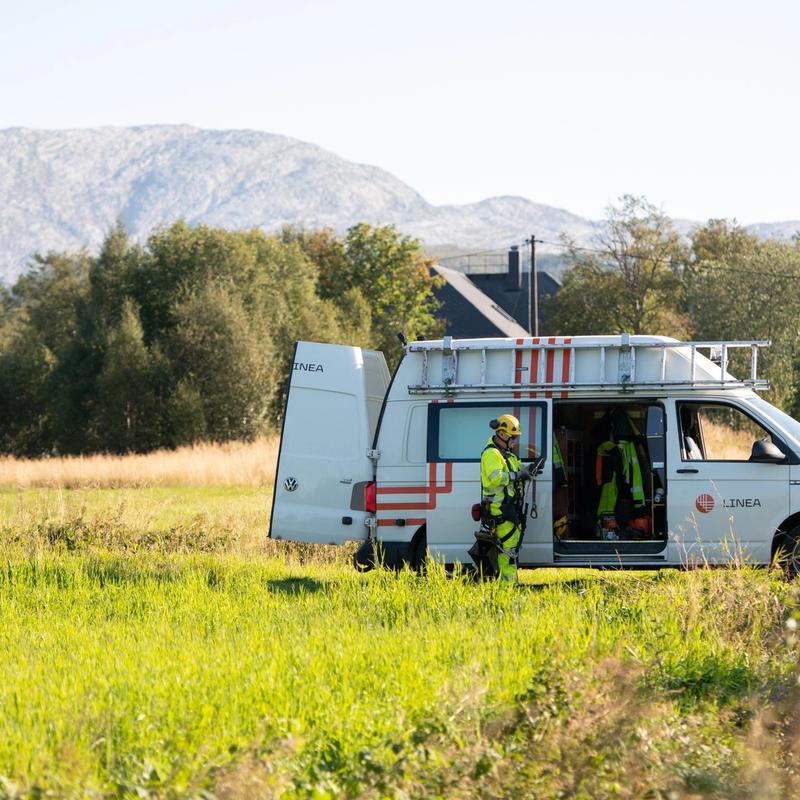 Bil fra Linea og montør som står ute på gresset ved skogen.