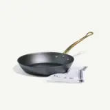 A black frying pan with a golden handle sits next to a folded kitchen towel.