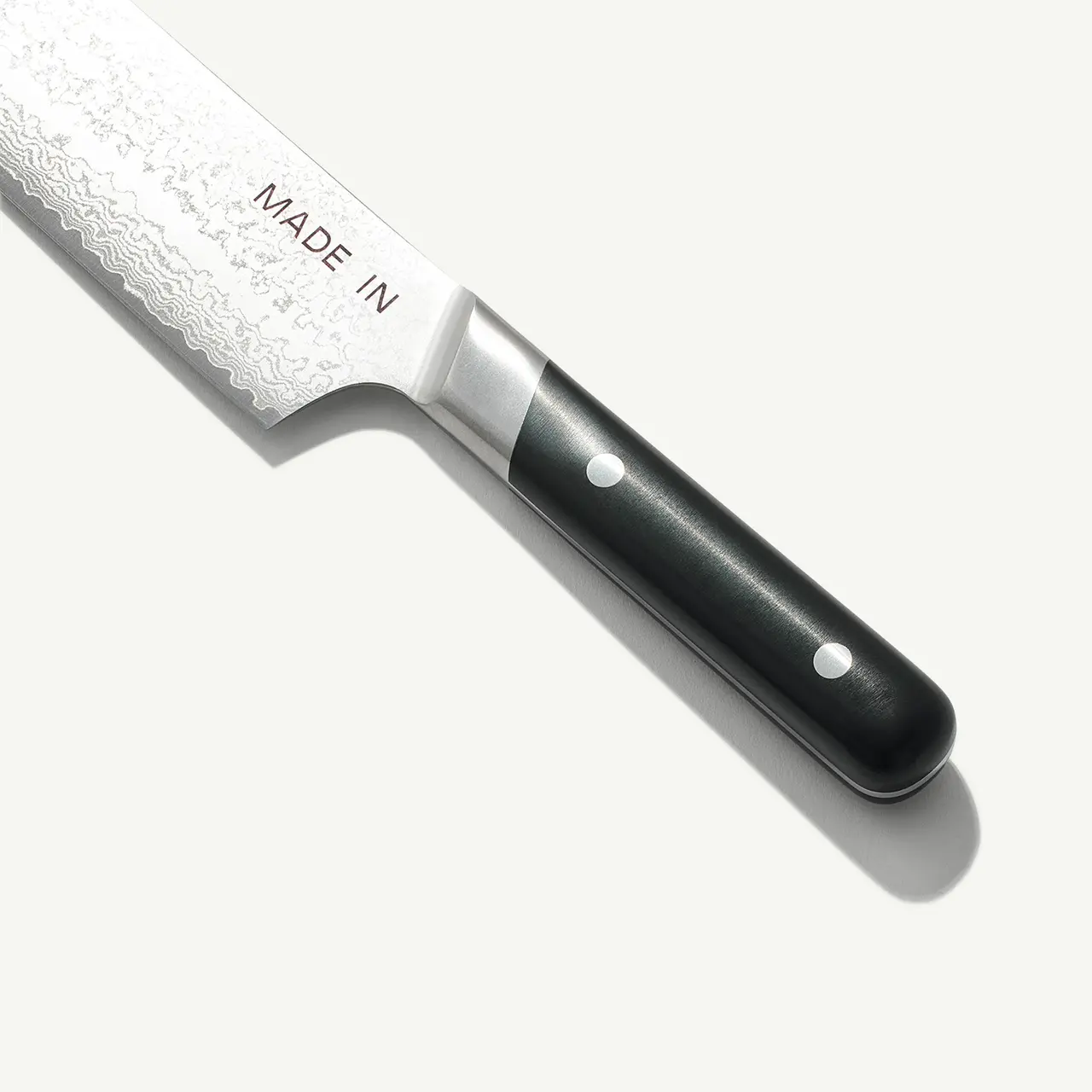 A close-up view of a chef's knife with a black handle and the words "MADE IN" engraved on the blade.