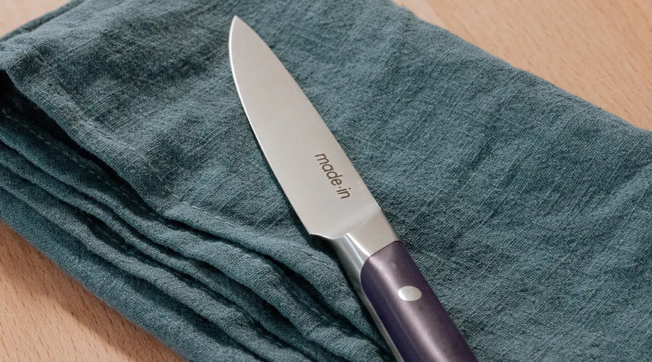 A kitchen knife lies on a teal cloth napkin set against a wooden surface.