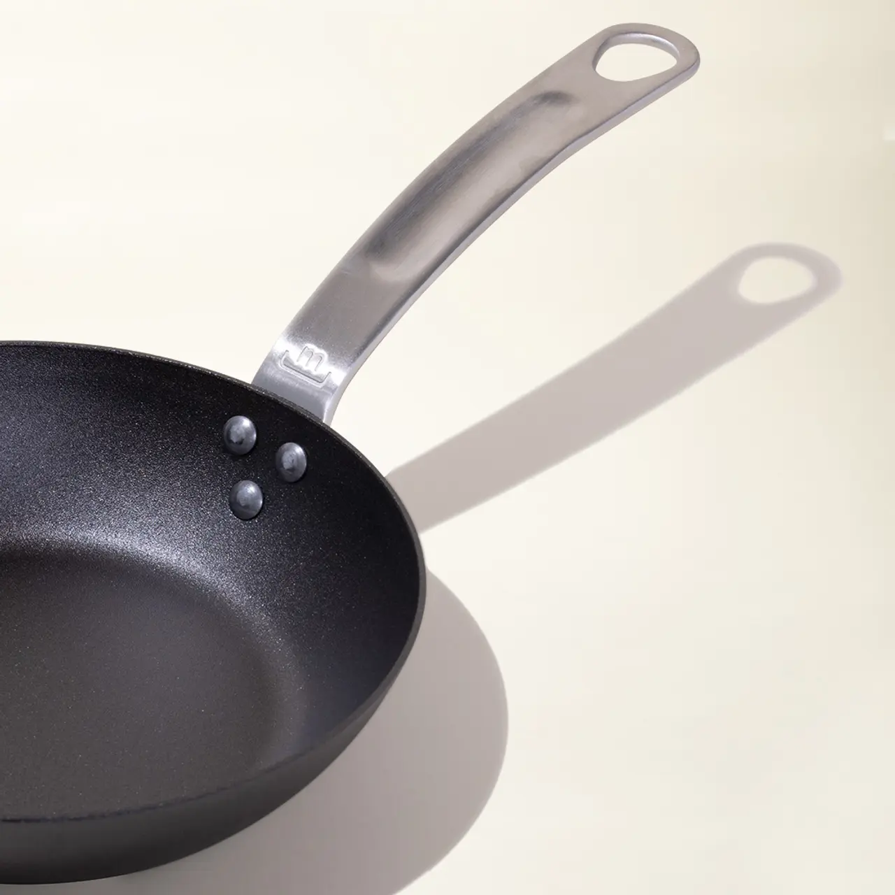 A frying pan casts a shadow on a light surface, suggesting it is placed under a focused light source.