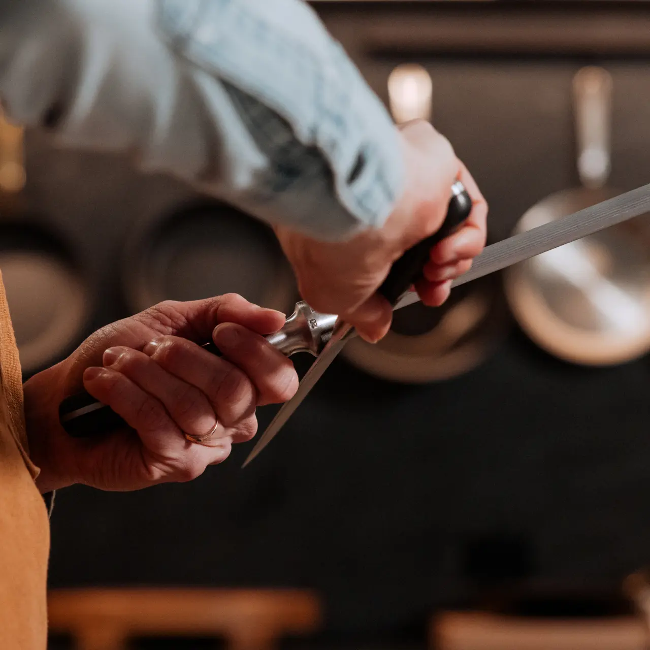 A person sharpens a knife with a honing tool in a kitchen setting.