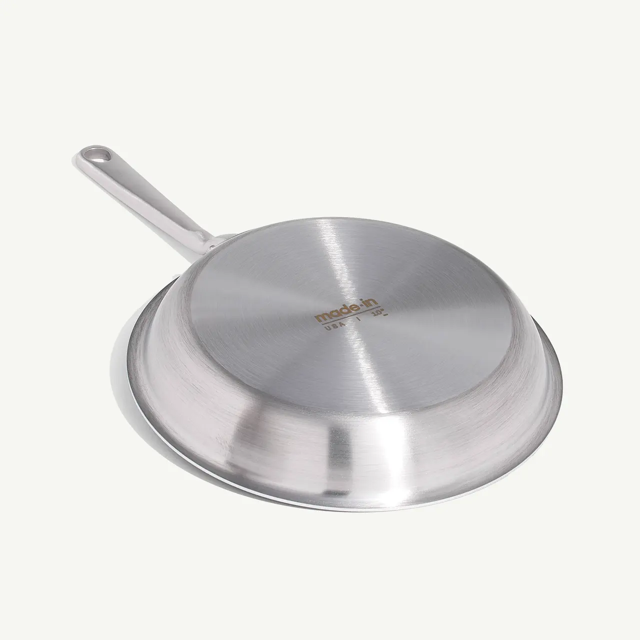 A stainless steel frying pan is displayed with its bottom facing up, showing the manufacturer's logo.