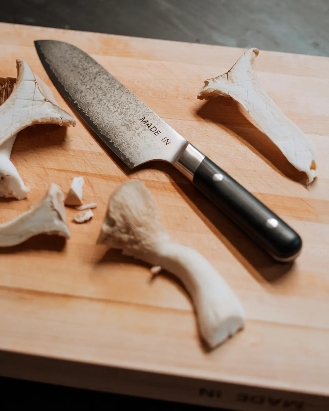 A stainless steel kitchen knife rests on a wooden cutting board beside sliced mushroom pieces.