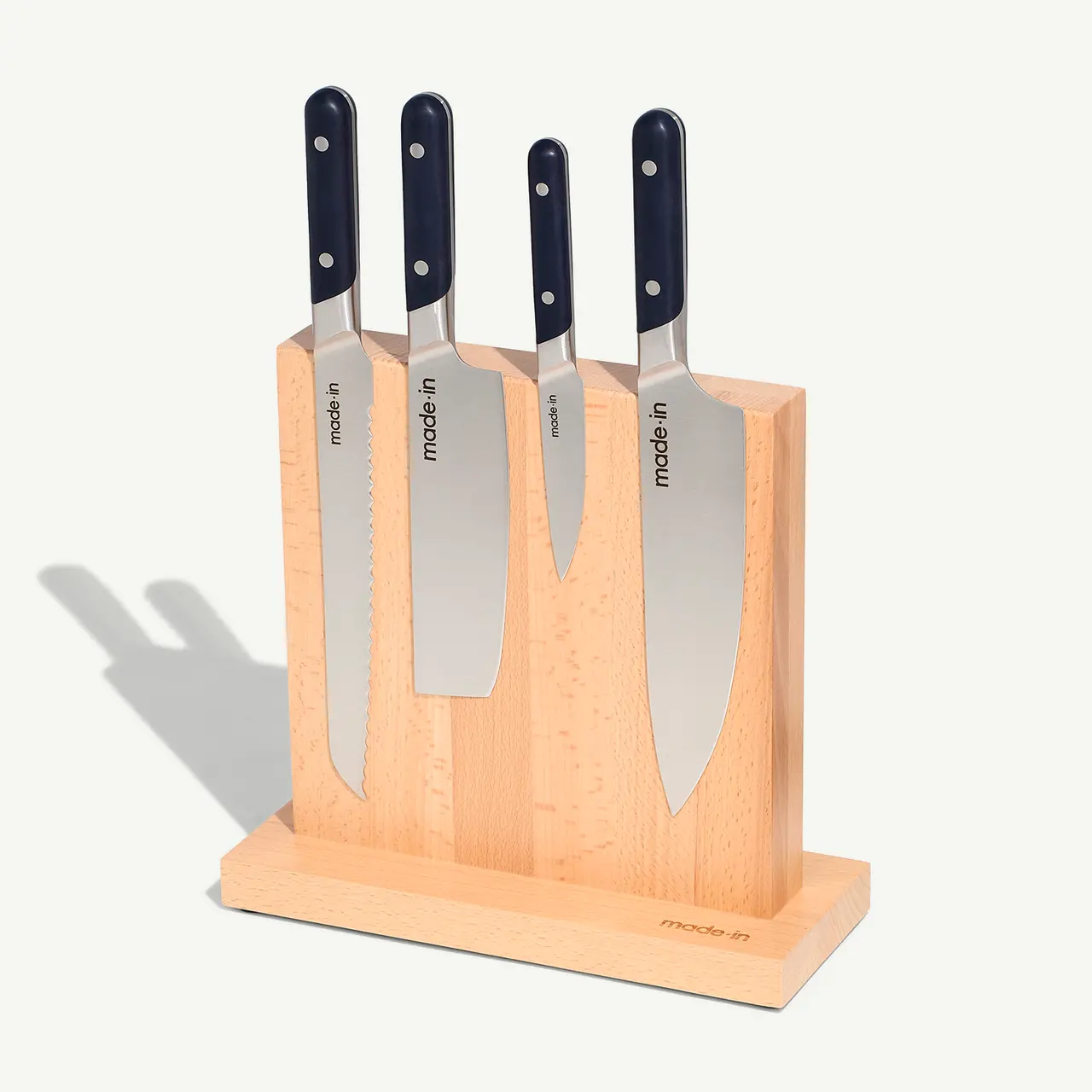 A set of four kitchen knives with dark handles is neatly arranged in a wooden block stand, casting a slight shadow on the right side.