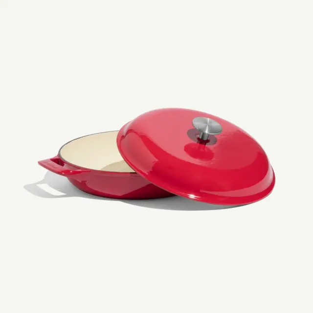 A bright red, enamel-coated Dutch oven with a matching lid slightly ajar.