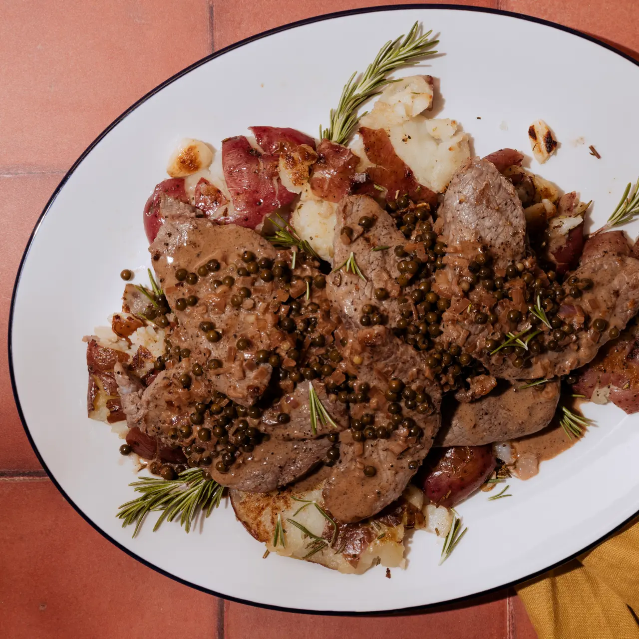 A plate of sliced beef with a peppercorn sauce, garnished with herbs, presented on a white-rimmed plate.
