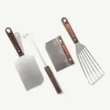 A set of four grilling tools, including a spatula, scraper, grill brush, and a steel spatula, all featuring wooden handles.