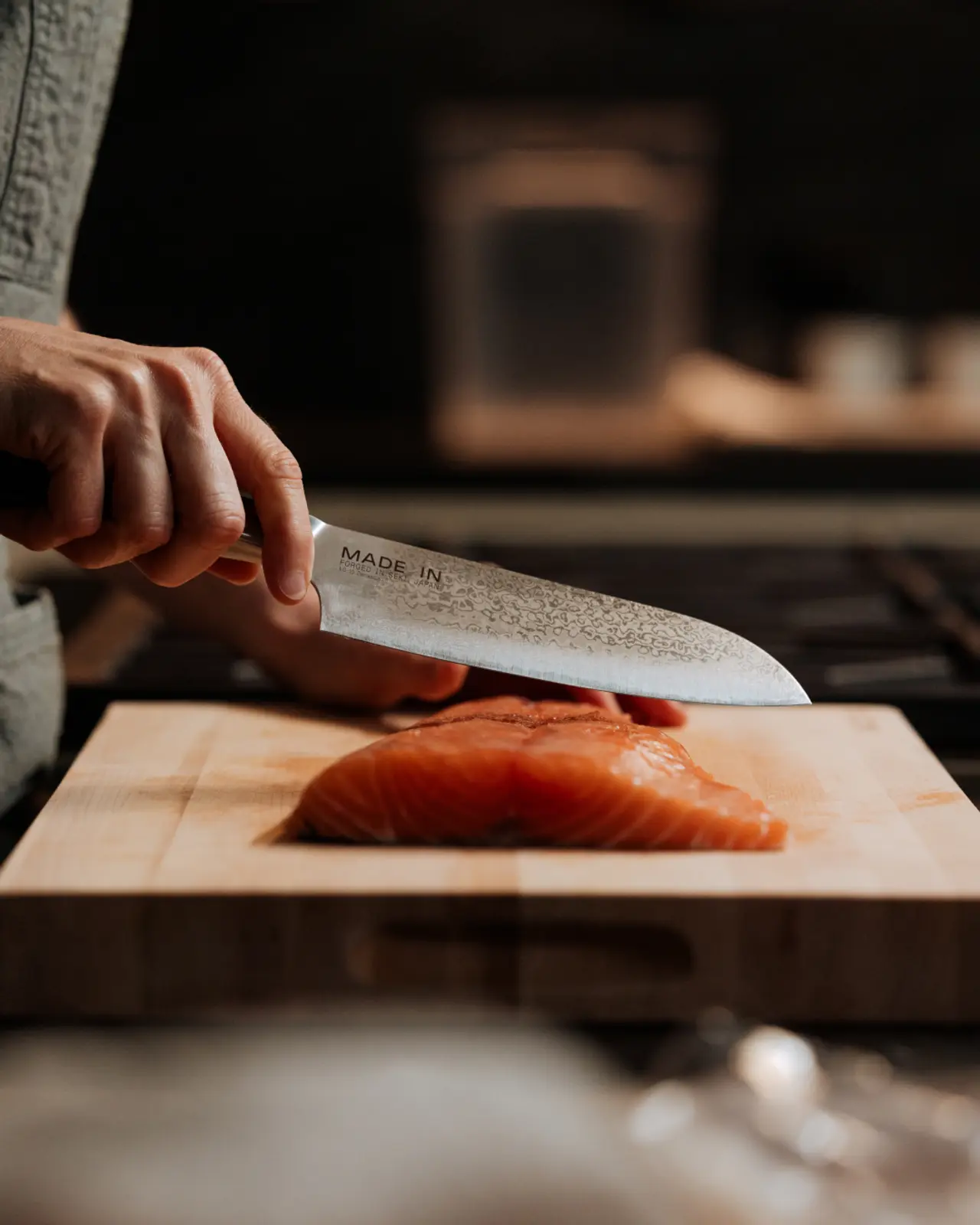 A person is slicing a piece of raw salmon on a wooden cutting board with a knife.