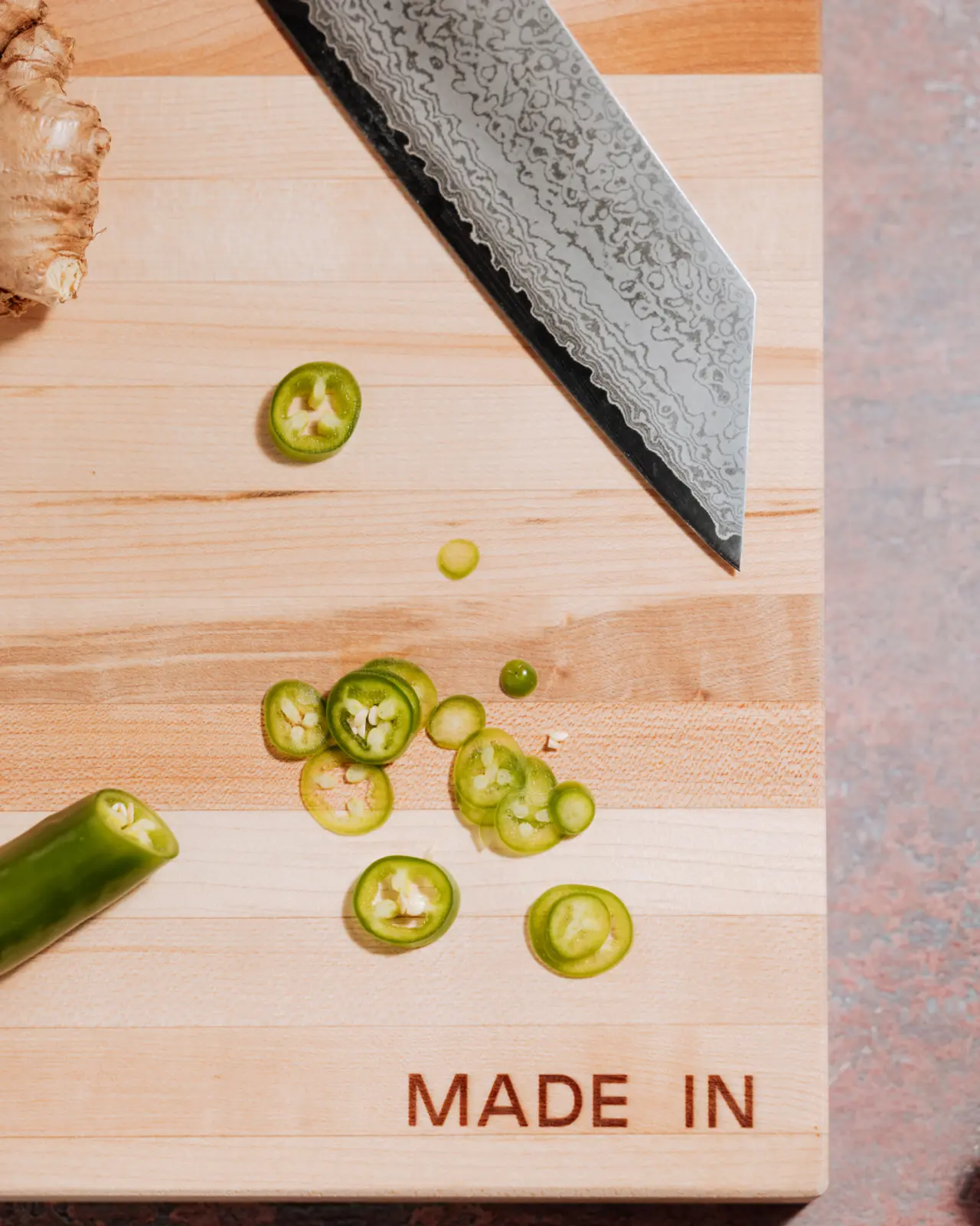 Sliced green jalapeños rest beside a chef's knife on a wooden cutting board stamped with "MADE IN."